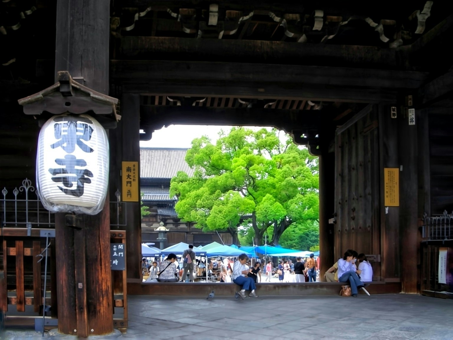 Vue à travers une porte de temple traditionnelle avec un grand arbre et des gens à l'extérieur