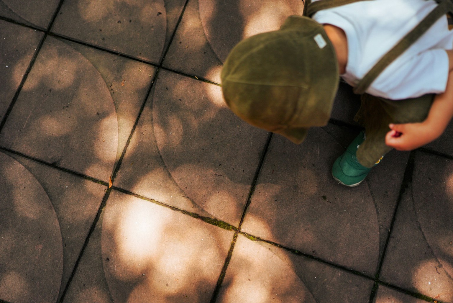 Ein Kind mit einem Hut schaut auf den Boden mit Lichtschatten auf den Fliesen