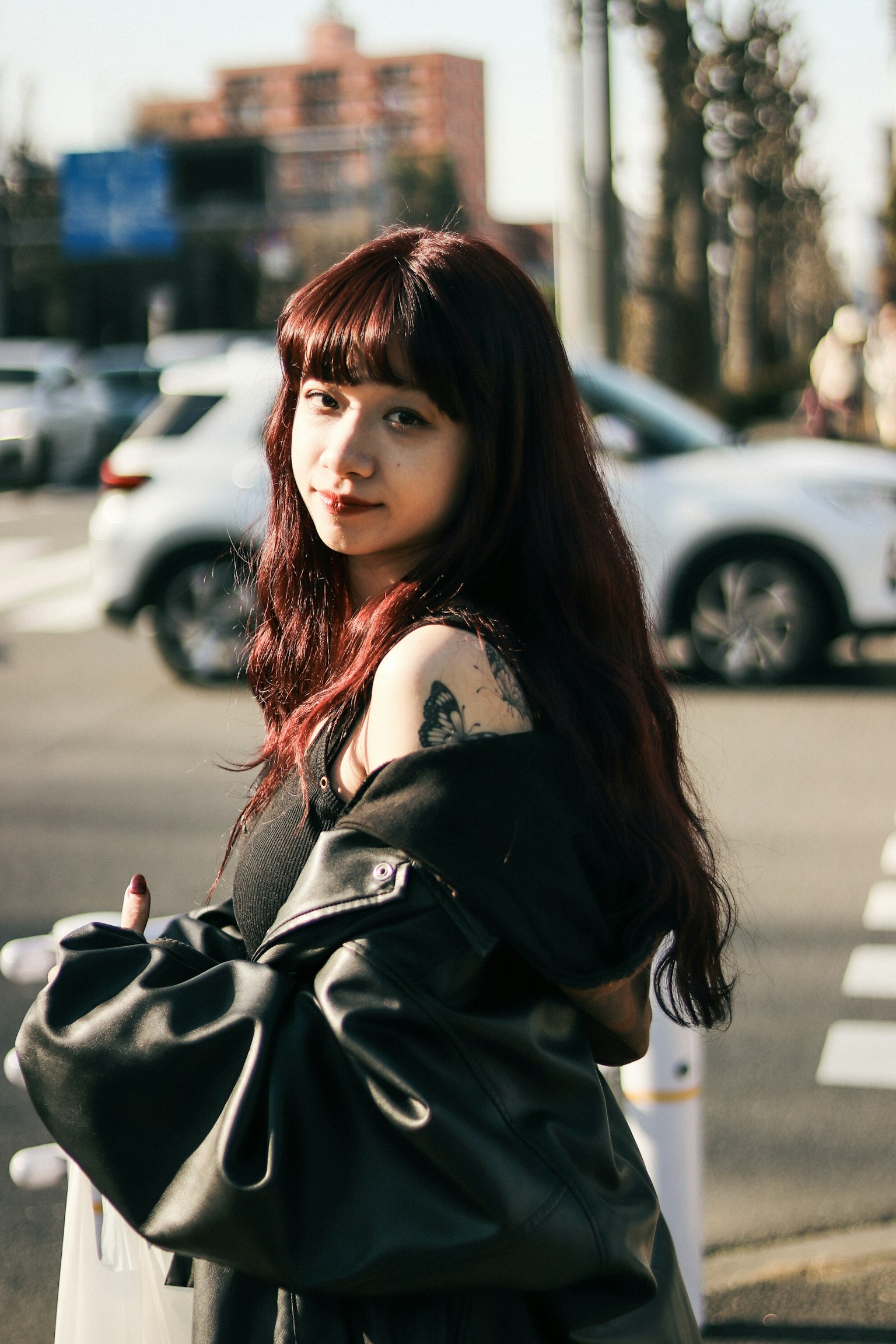 Mujer con cabello rojo oscuro largo usando una chaqueta negra mirando hacia atrás en un entorno urbano