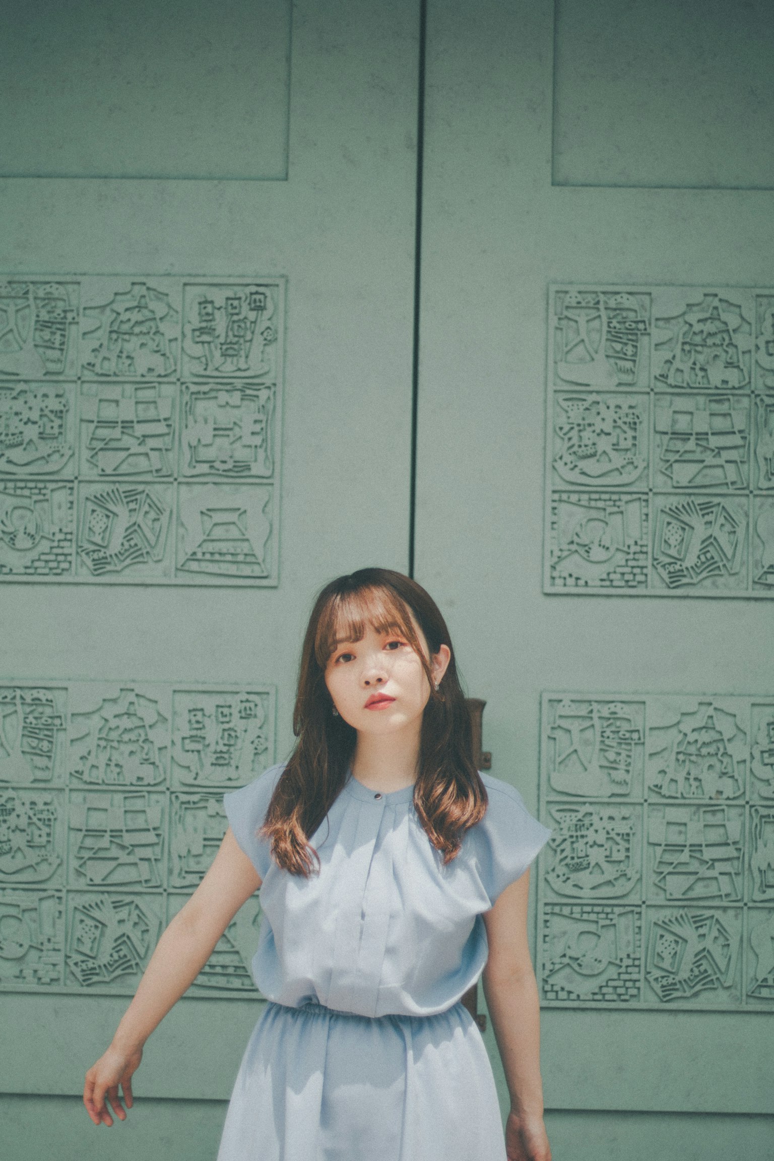 파란 드레스를 입은 여성이 조각이 있는 초록색 문 앞에 서 있다