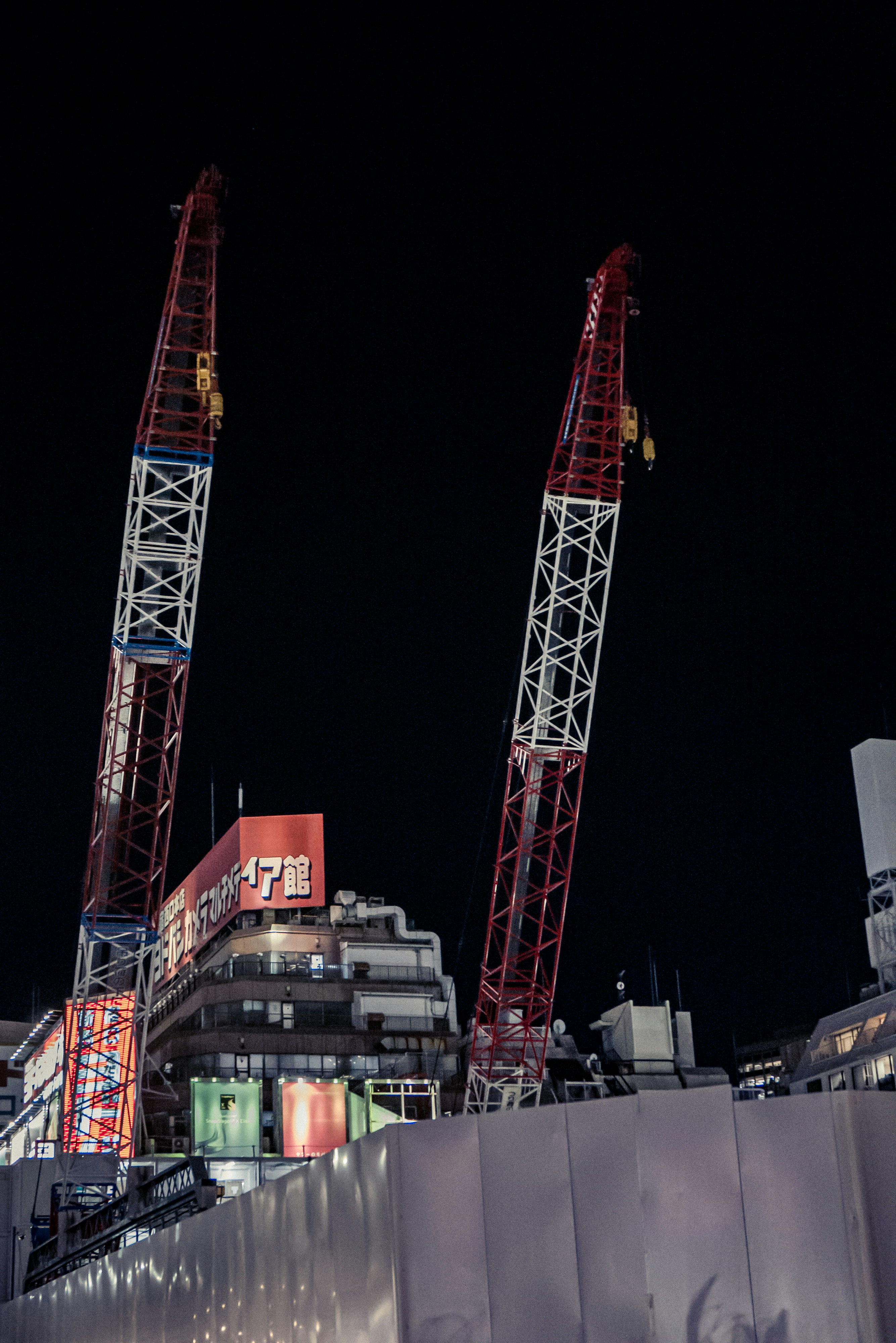 Night construction site with towering cranes and surrounding buildings