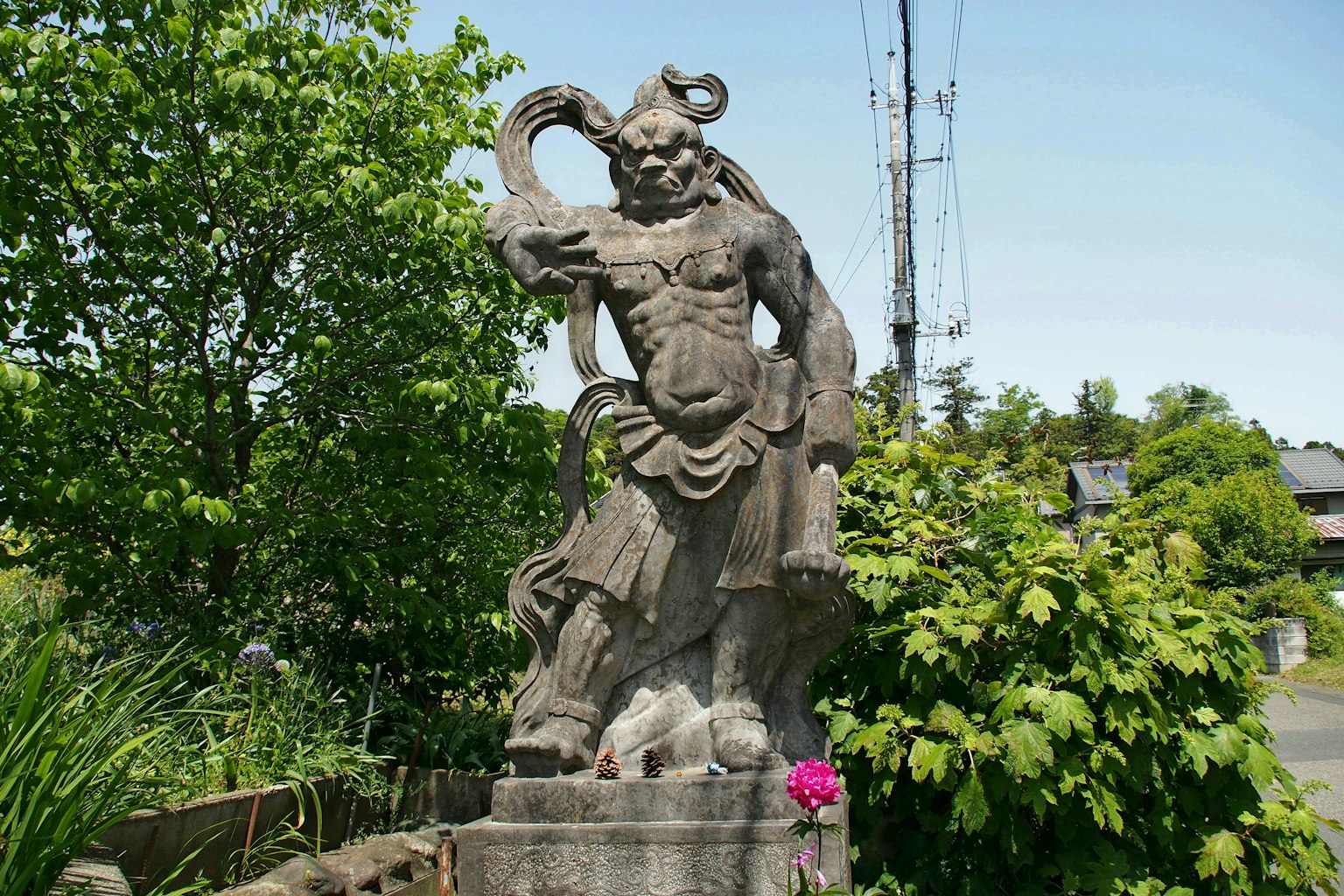 Una estatua de piedra de una deidad masculina sosteniendo una espada se erige rodeada de vegetación