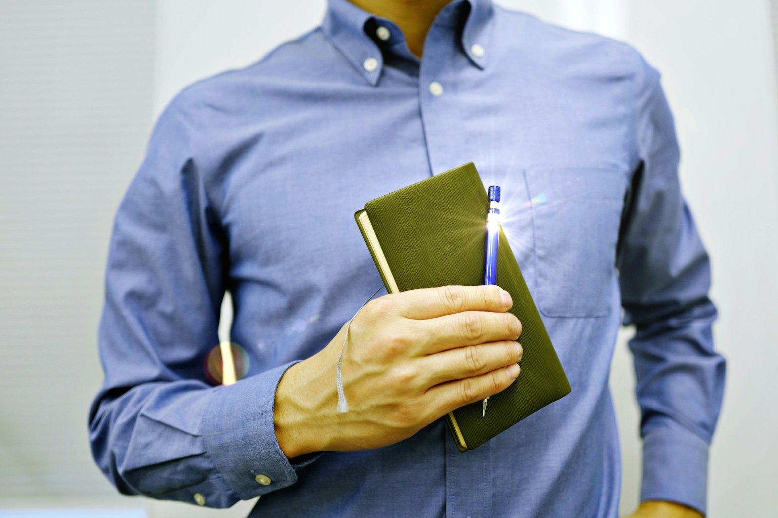 Uomo in camicia blu che tiene un quaderno verde e una penna