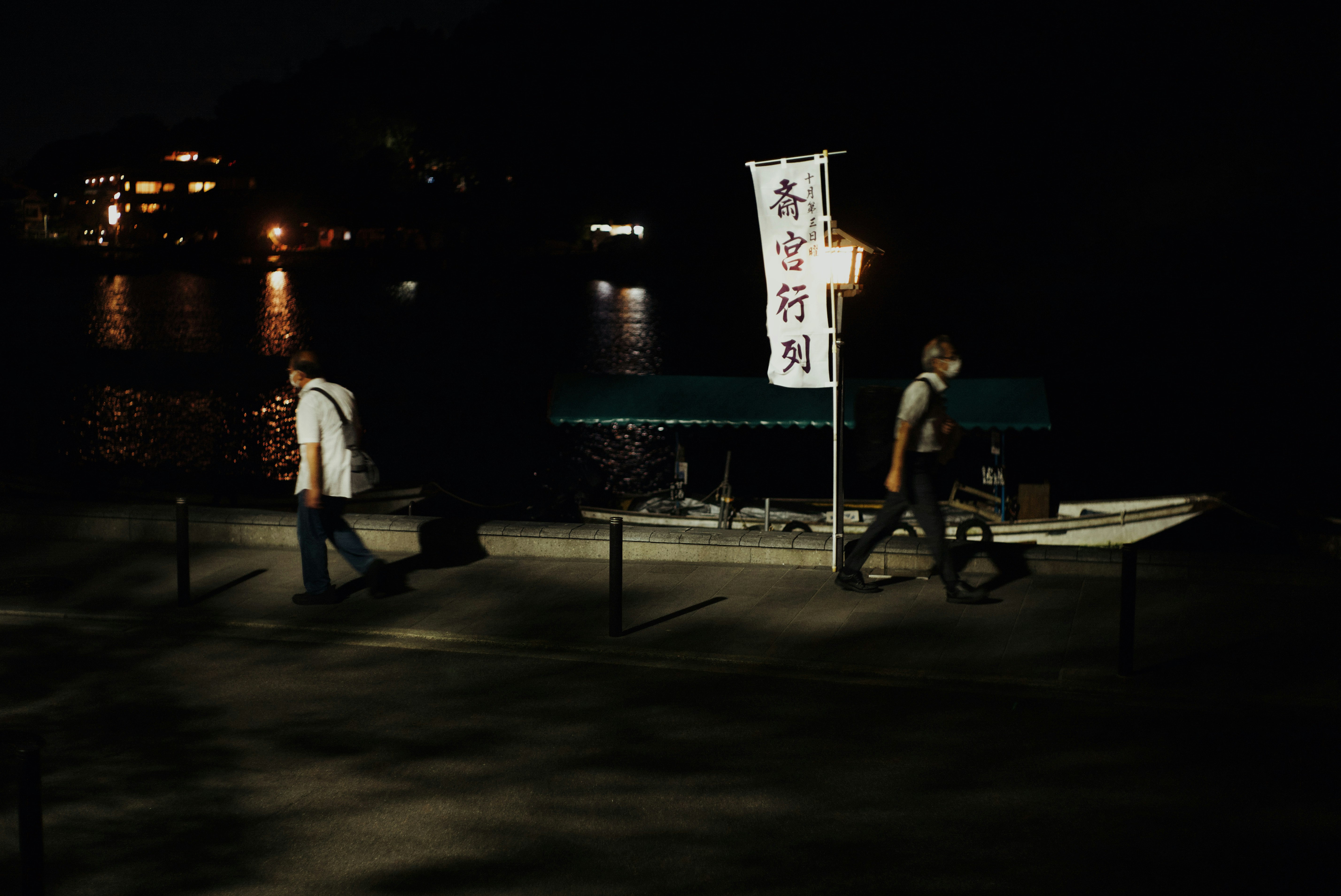 夜の川沿いで提灯の看板を見上げる人々