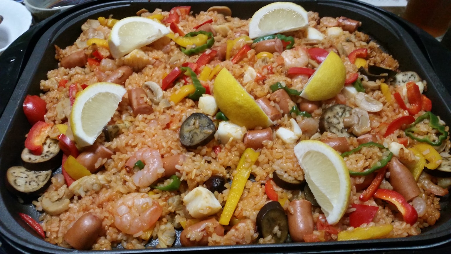 Paella ricca di frutti di mare e verdure guarnita con fette di limone