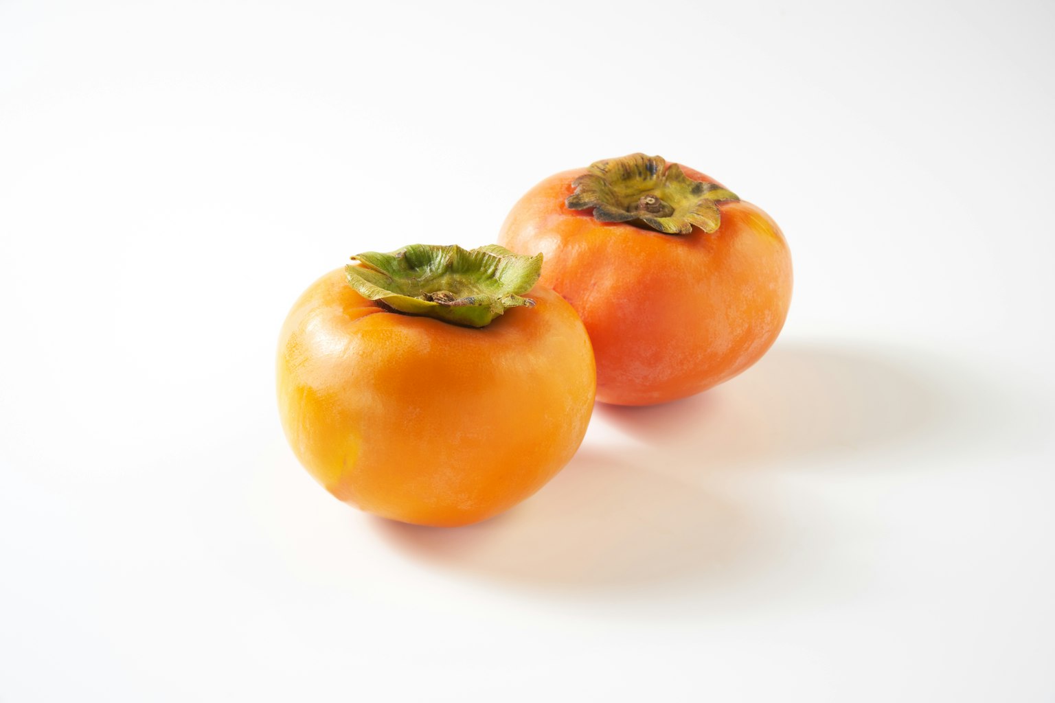 Zwei orangefarbene Persimonen auf einem weißen Hintergrund