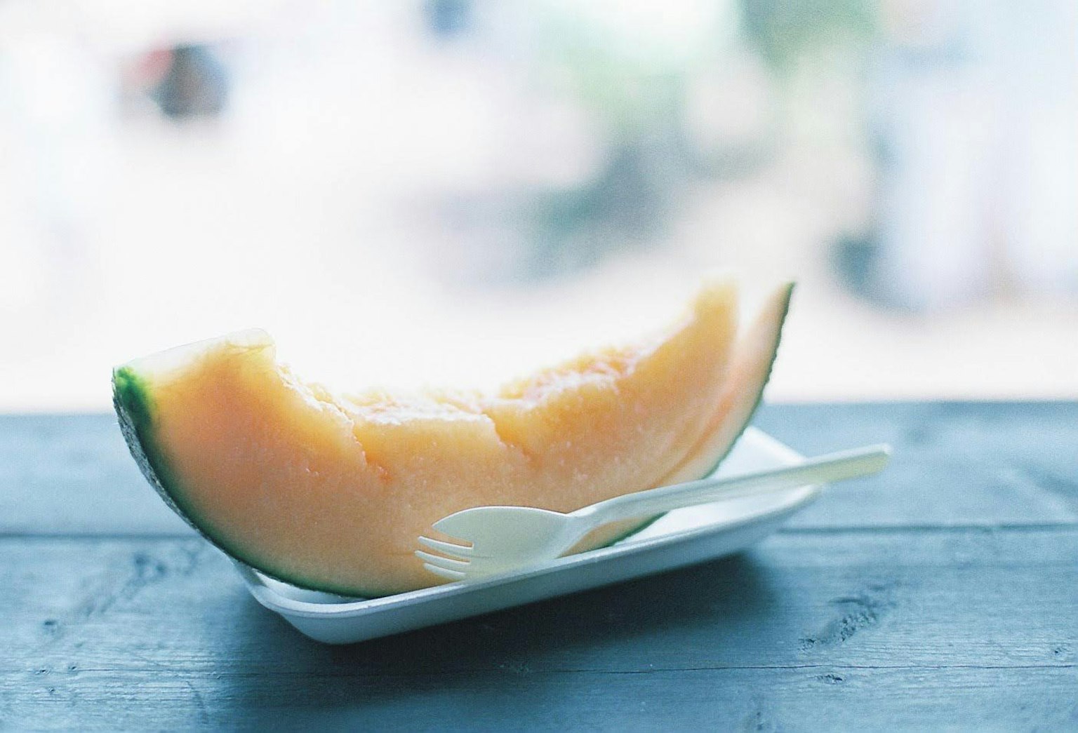 Una fetta di melone su un piccolo piatto bianco con un cucchiaio