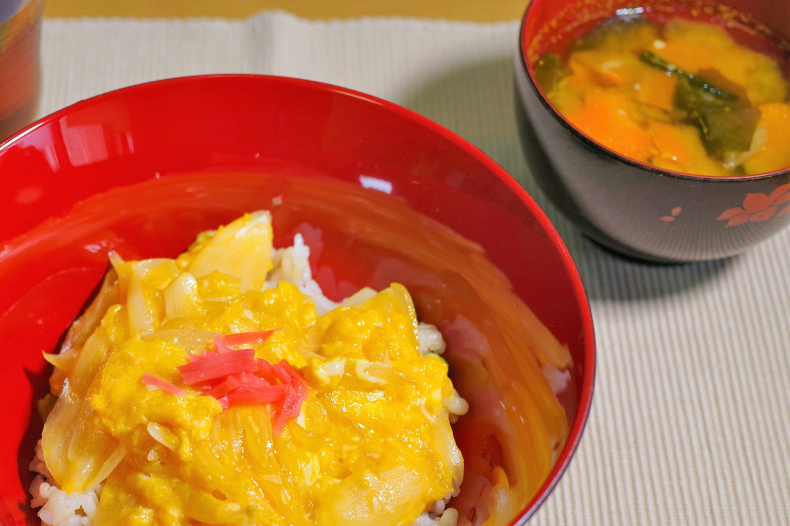 Un tazón de arroz con huevo decorado con jengibre encurtido y un tazón de sopa miso al lado