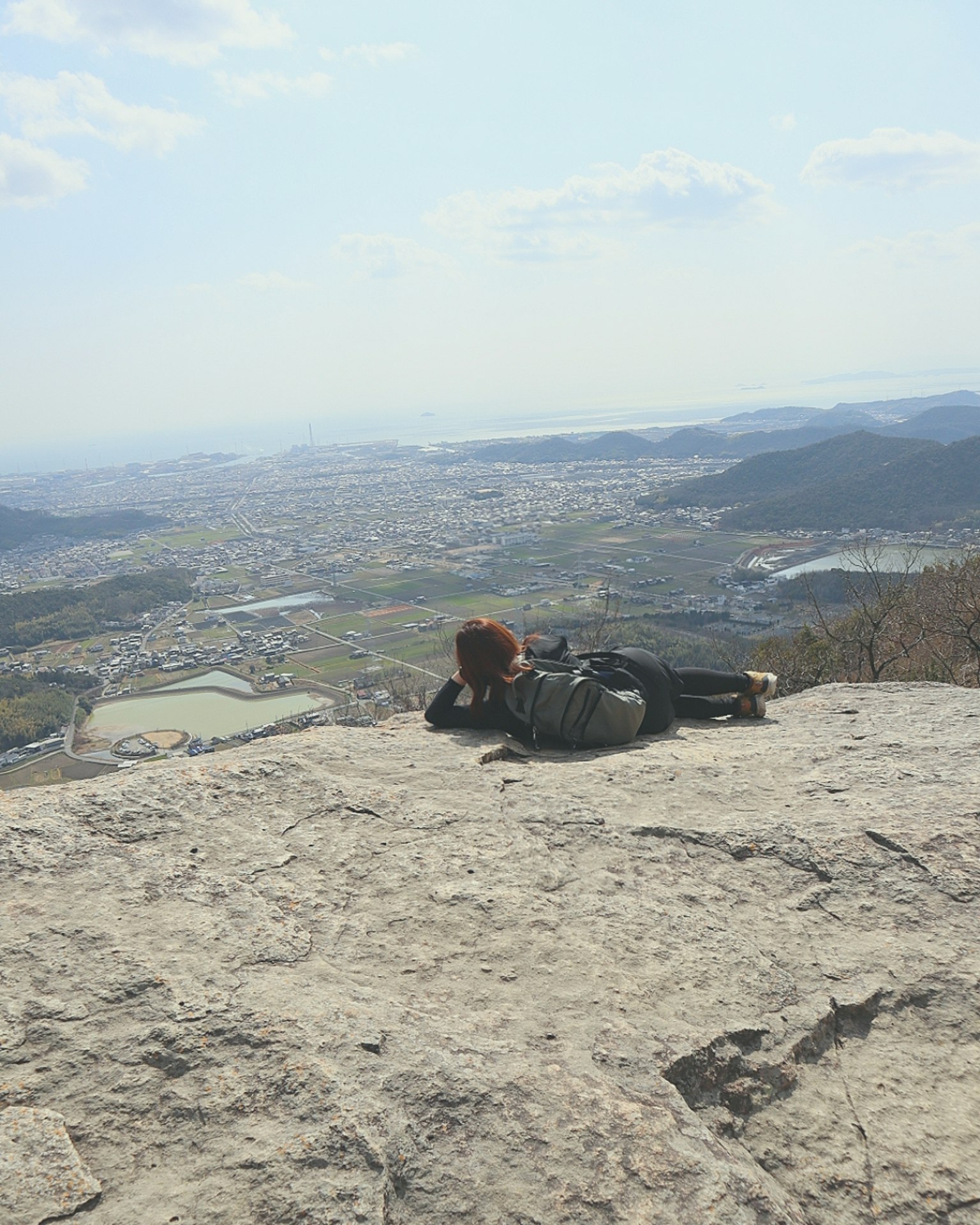 Person lying on a mountain top overlooking a scenic view