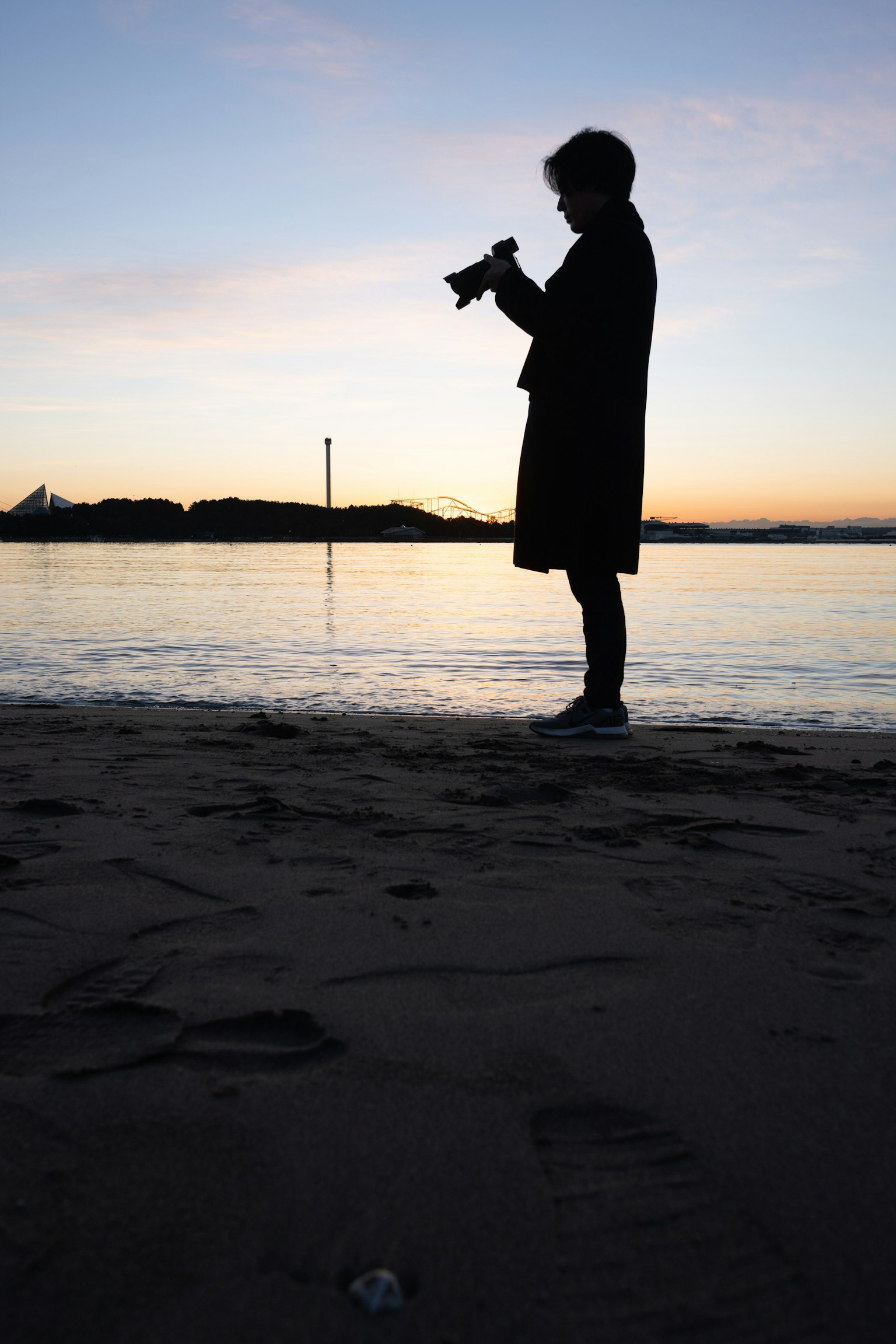 Silhouette di una persona che tiene una macchina fotografica sulla spiaggia al tramonto