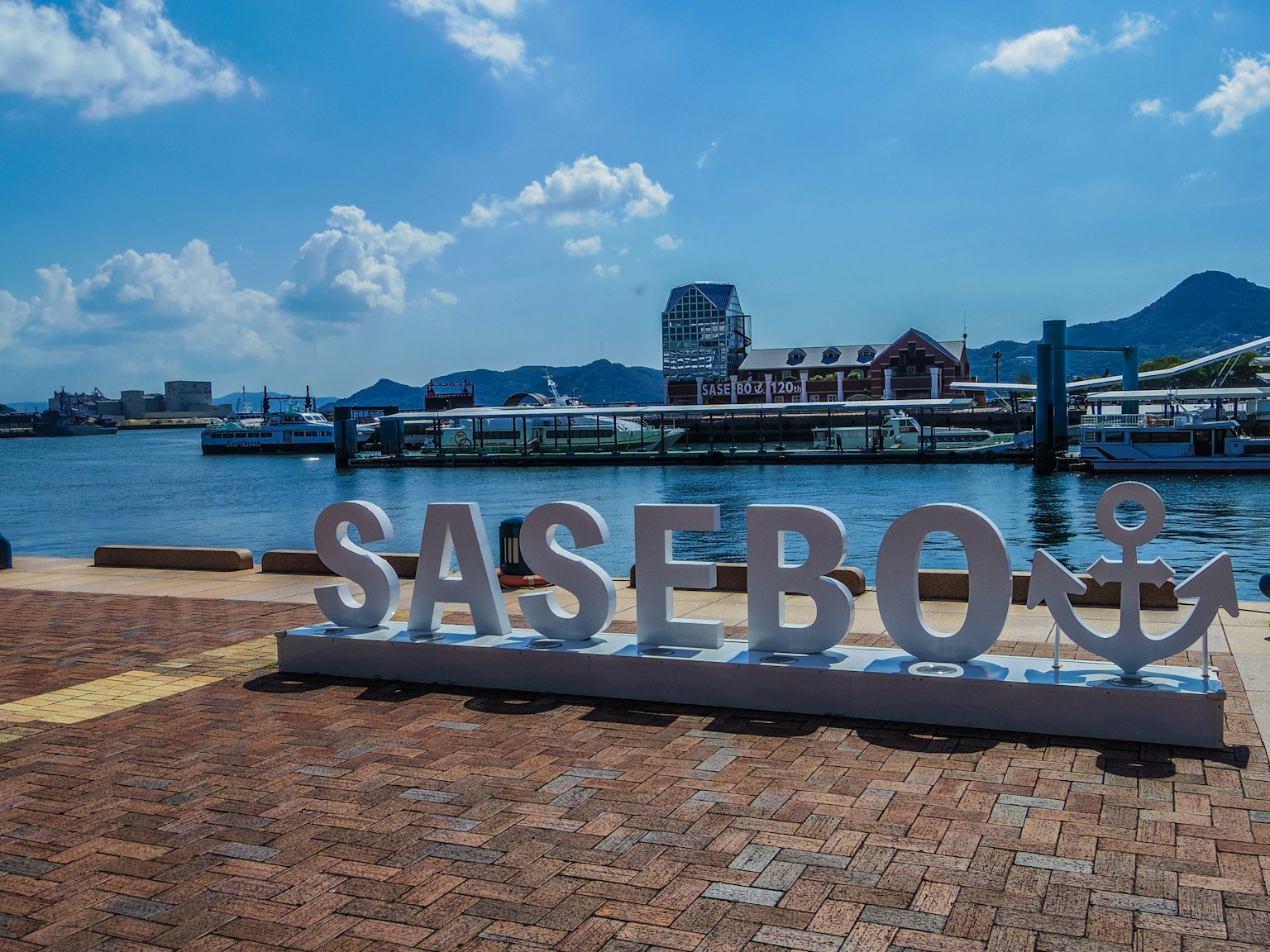 Großes Schild mit der Aufschrift SASEBO am Wasser unter blauem Himmel