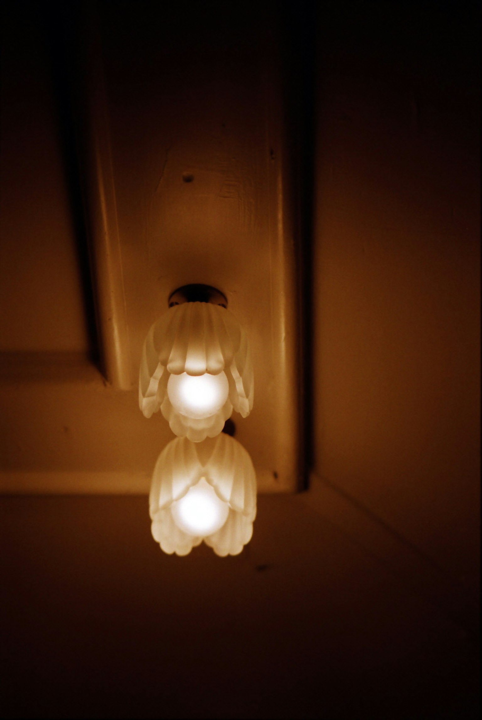 Gambar dua kap lampu putih tergantung dari langit-langit di ruangan yang redup