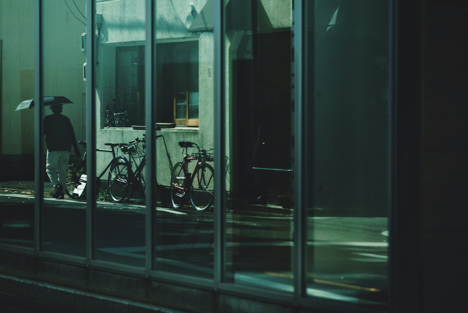 Une personne avec un parapluie se tient devant un verre réfléchissant aux côtés de bicyclettes