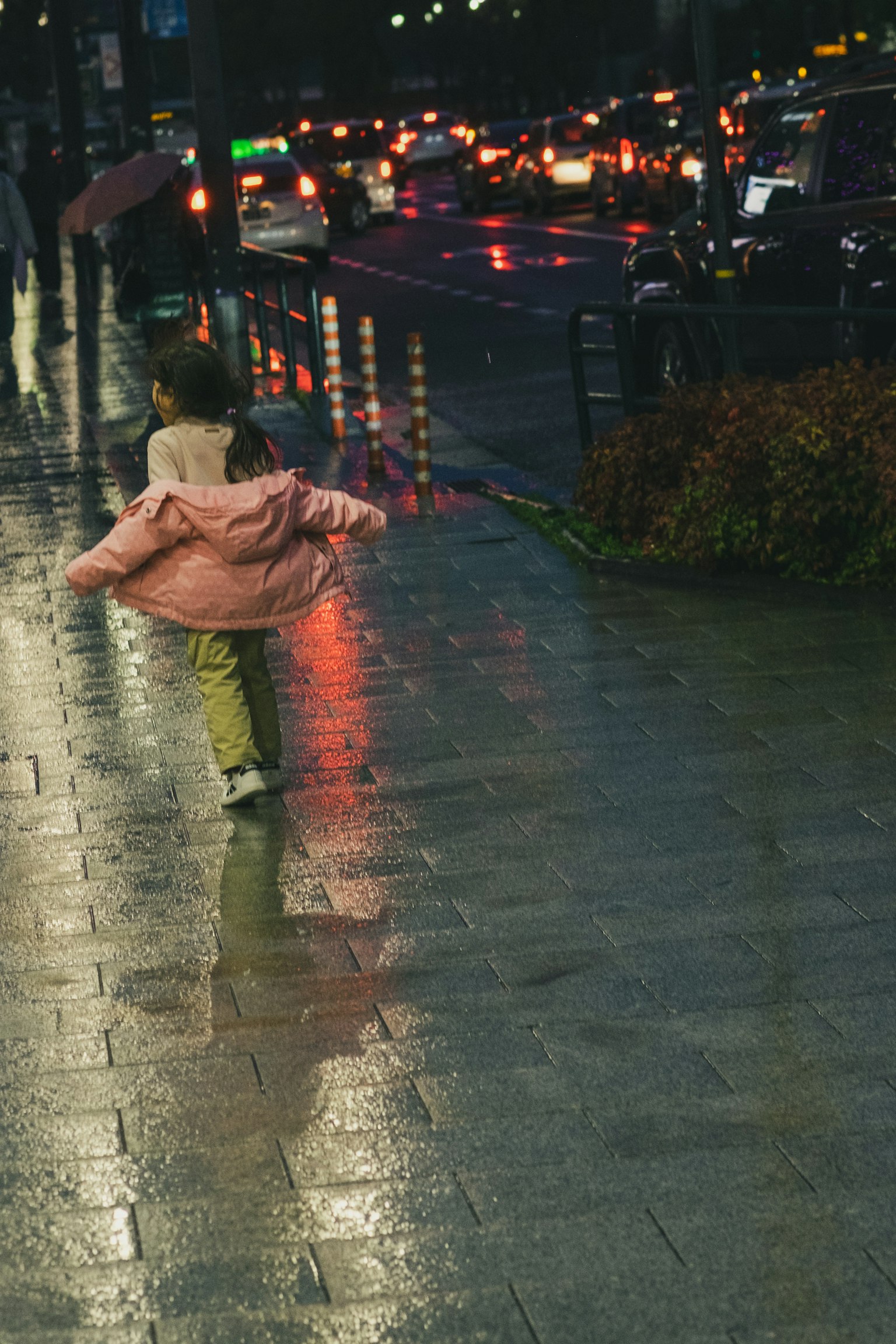 A child in a pink coat joyfully walking on a rainy street with reflections