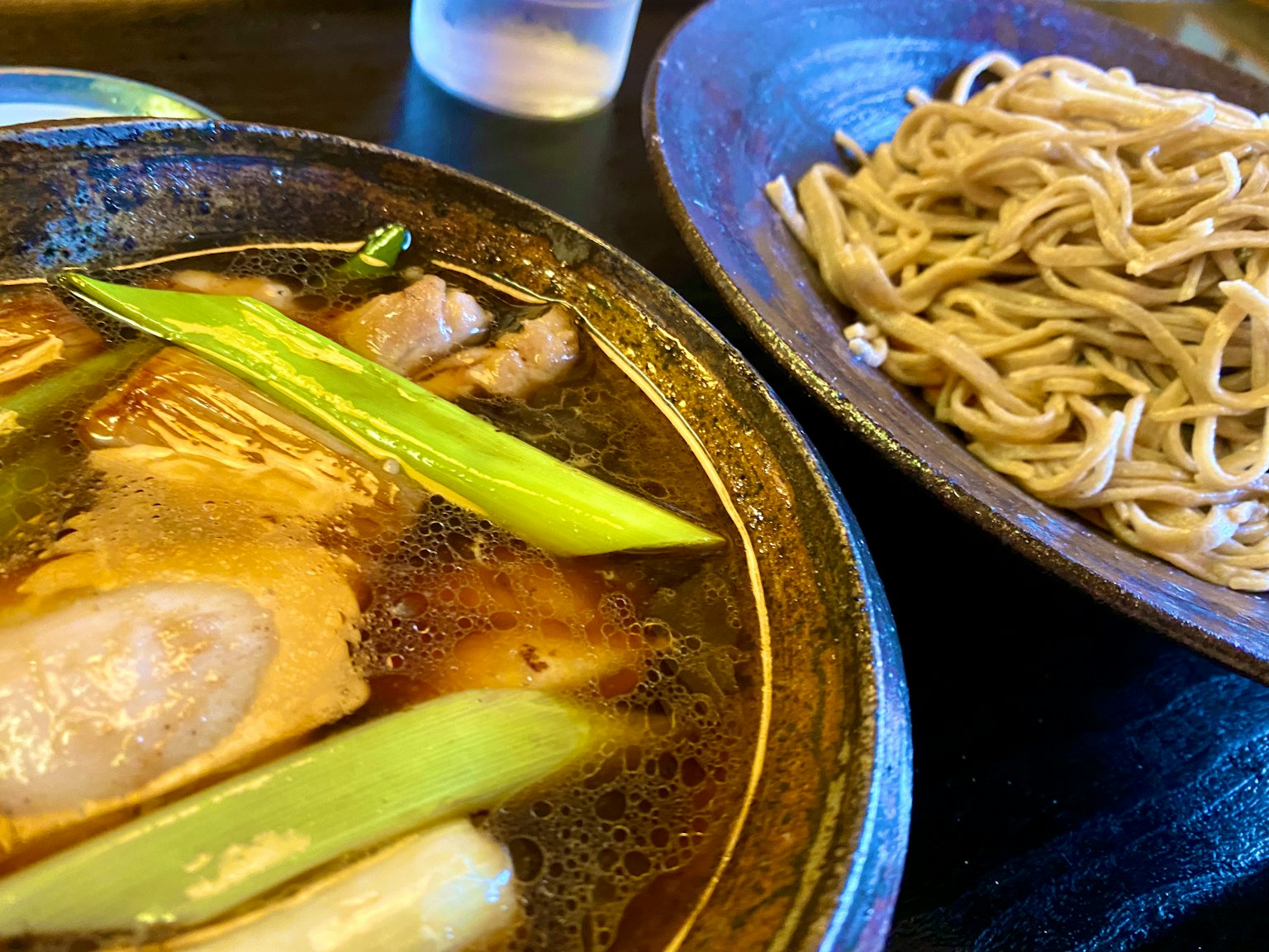 Một bát súp nóng với hành lá và thịt bên cạnh đĩa mì soba
