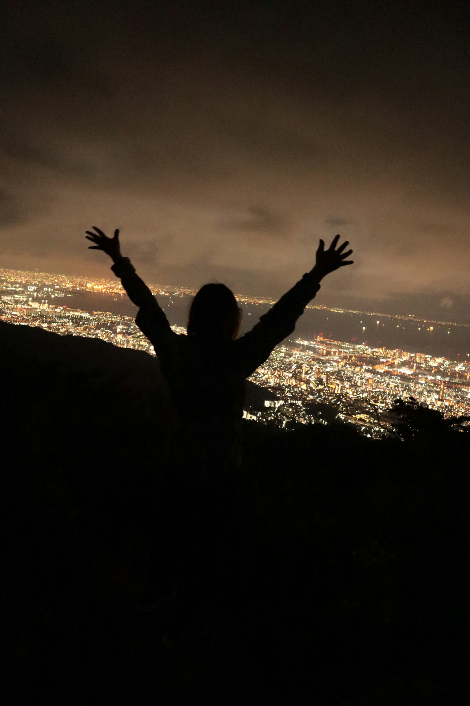 Silhouette einer Person mit erhobenen Armen vor einer nächtlichen Stadtlandschaft