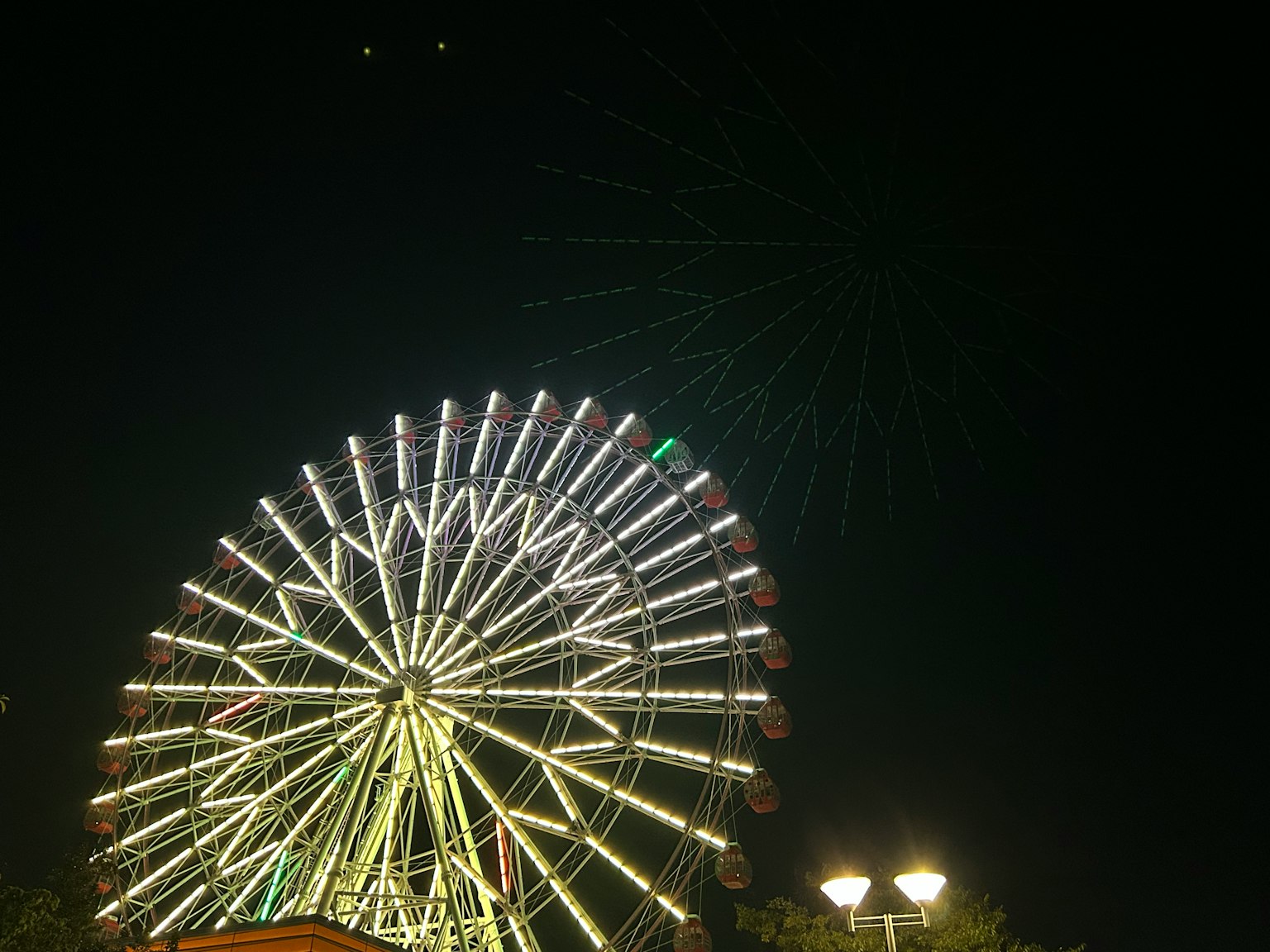 Beleuchtetes Riesenrad bei Nacht mit Feuerwerk im Hintergrund
