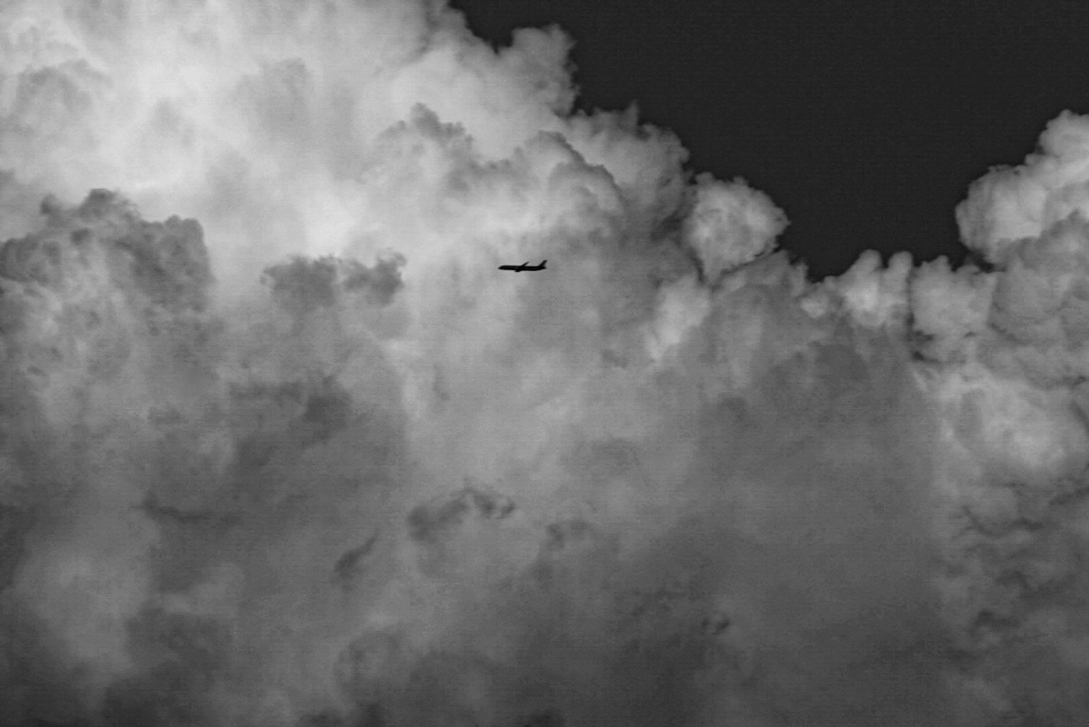 Foto in bianco e nero di un aereo che vola tra le nuvole