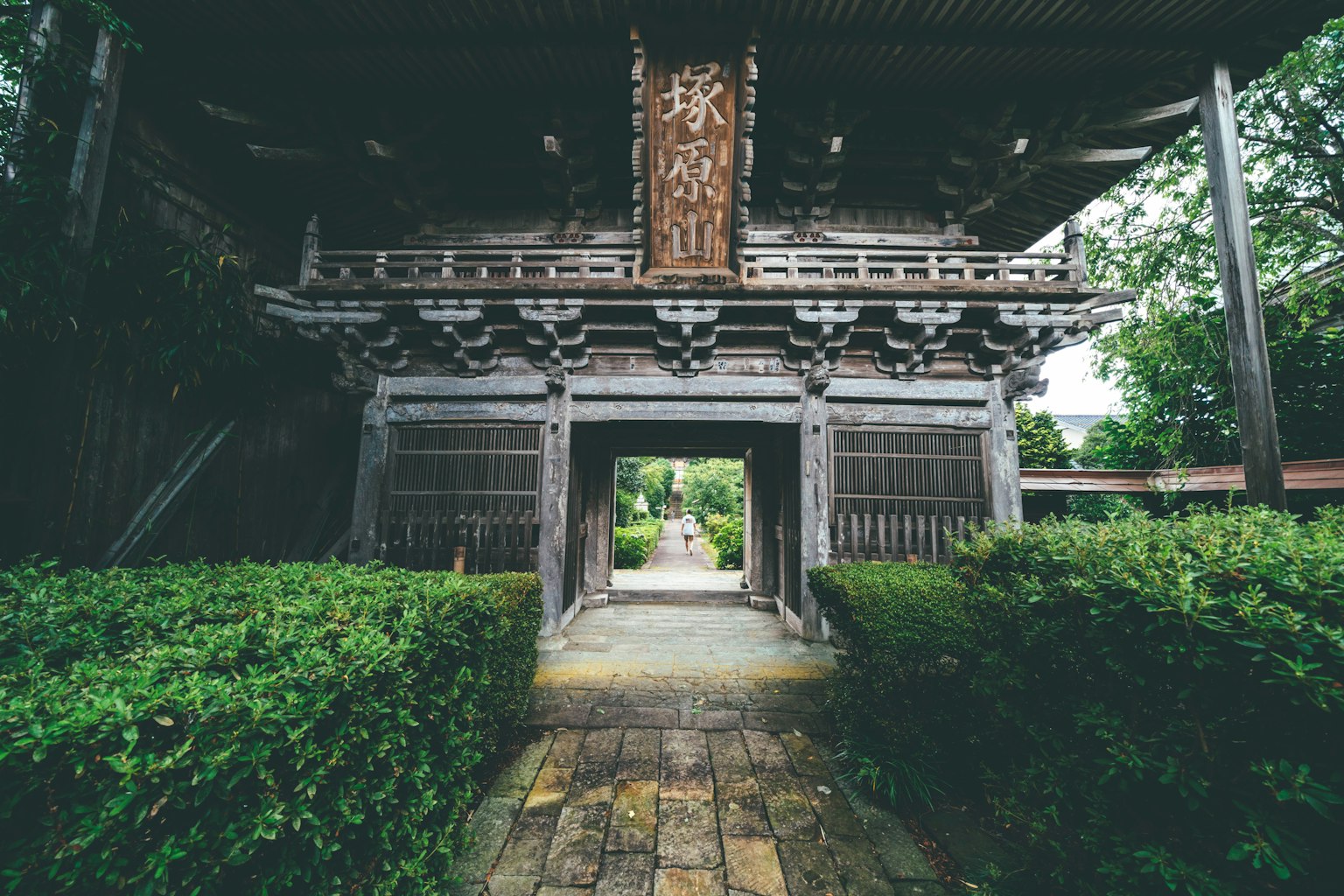 Puerta japonesa tradicional con vista al jardín que presenta vegetación y un camino de piedra
