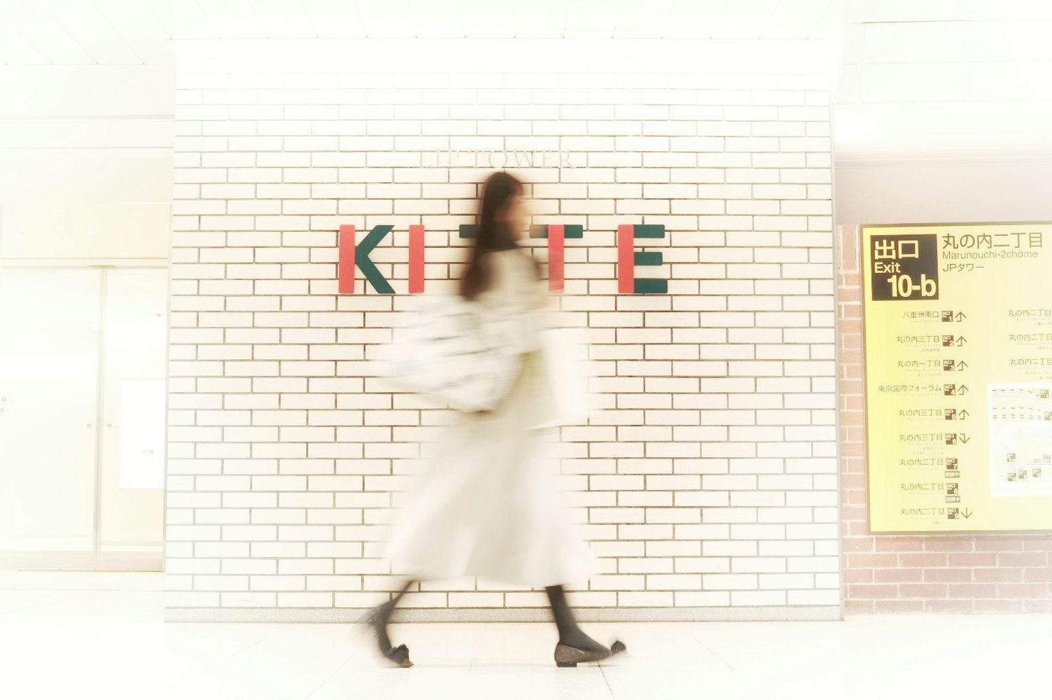 一名女性走过一面白色墙壁，上面有彩色字母拼成的KITE