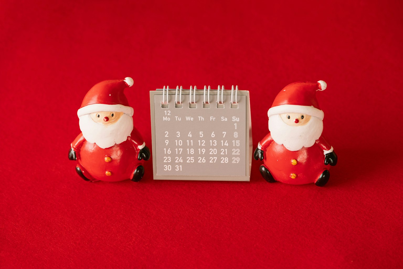 Figuras de Papá Noel sobre fondo rojo con un calendario en el medio
