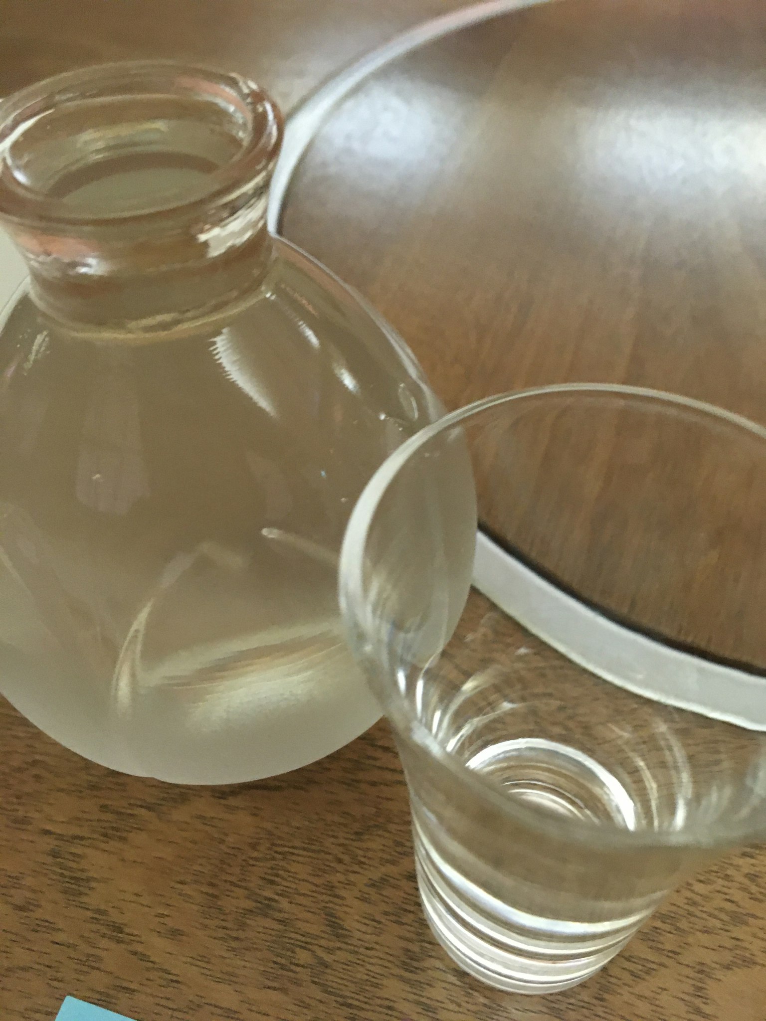 Sebuah gelas berisi air jernih di samping botol kecil di atas meja kayu