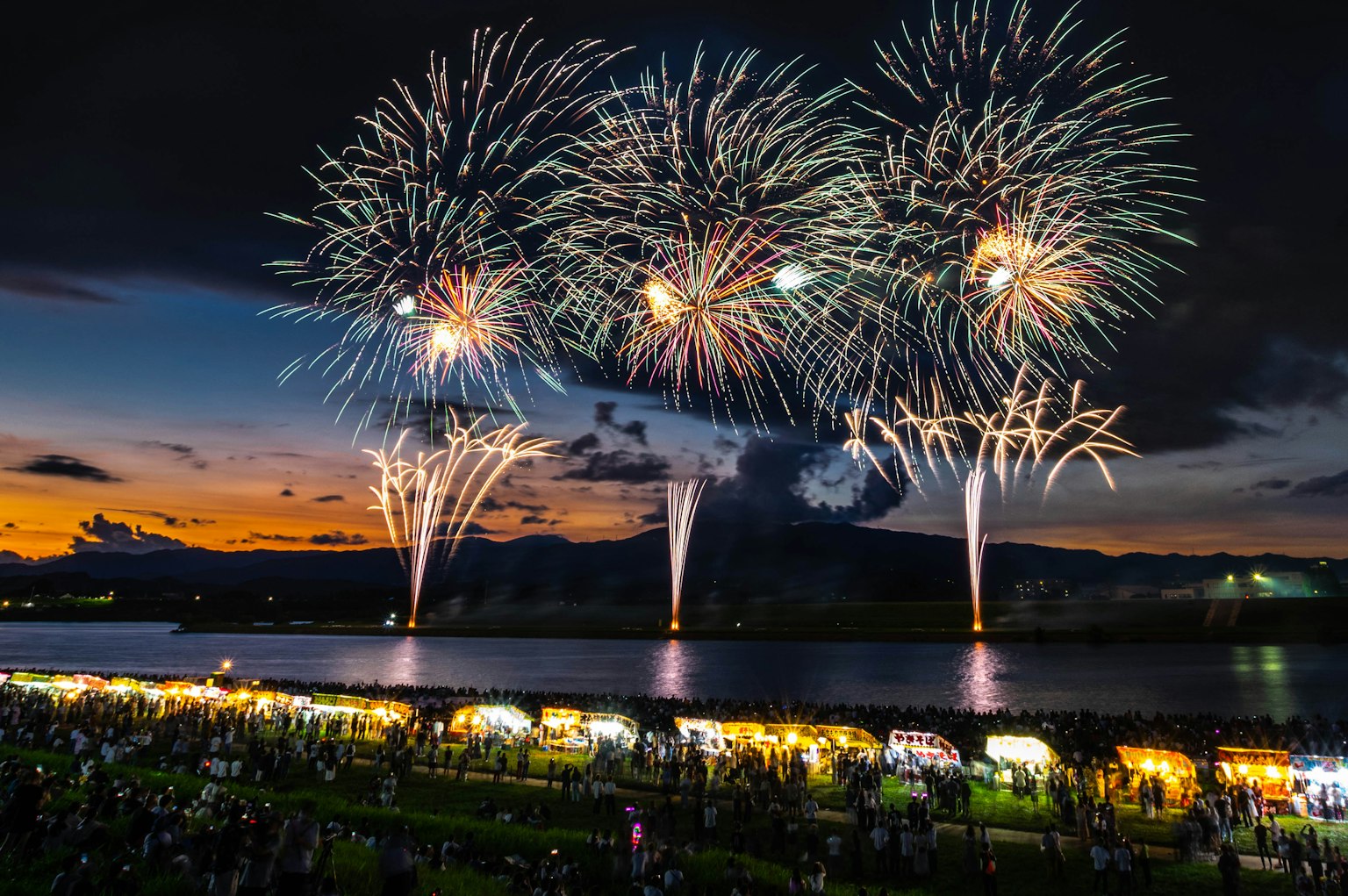 Des feux d'artifice illuminent le ciel nocturne au-dessus d'une rivière avec des foules rassemblées en dessous