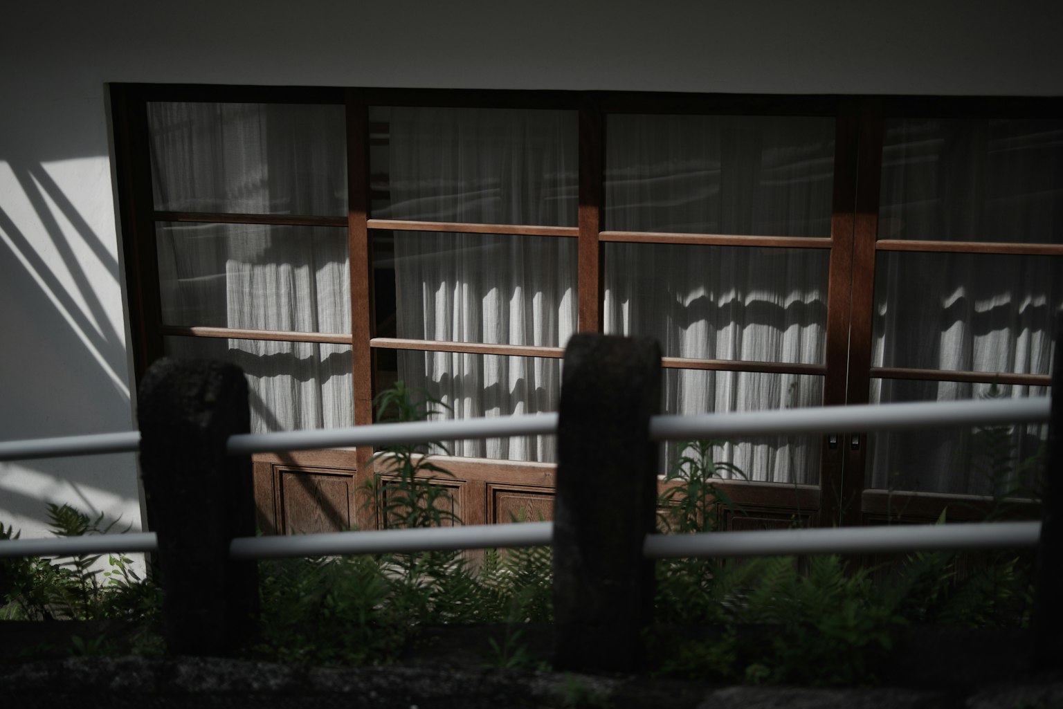 Vista lateral de un edificio con ventanas de madera y cortinas rodeado de vegetación