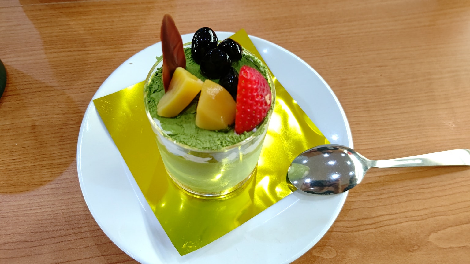 Cangkir dessert matcha yang dihiasi dengan berbagai buah yang disajikan dengan indah