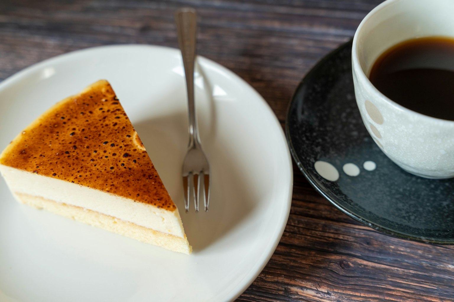 ชิ้นเค้กชีสครีมและถ้วยกาแฟบนโต๊ะ