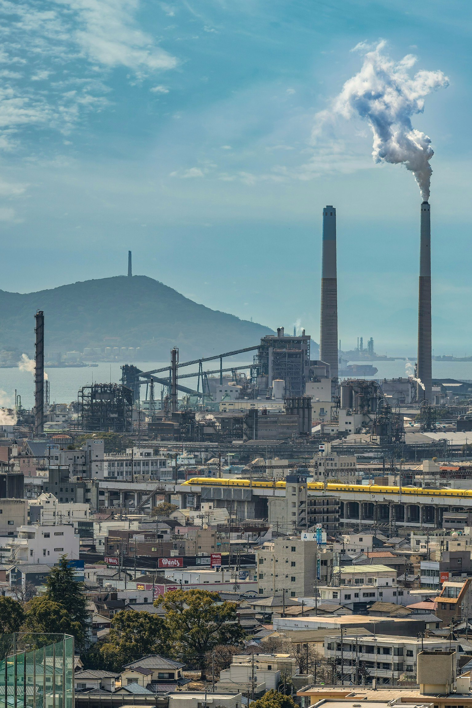 ドクターイエローと工場群の煙突が見える工業地帯の風景