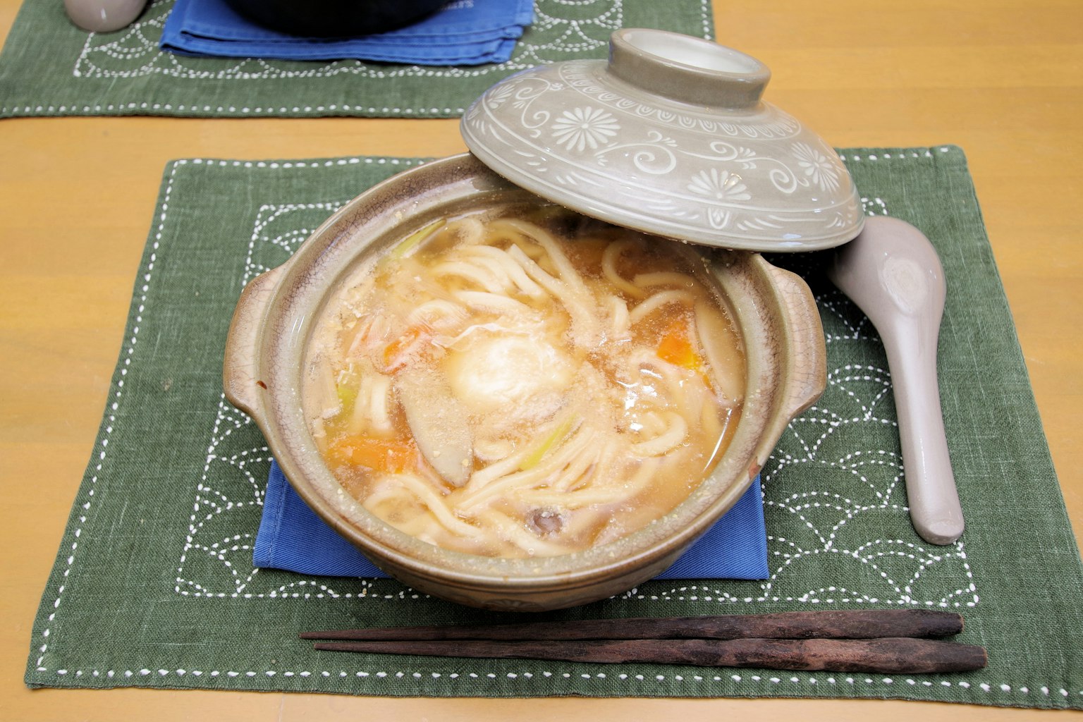 Hidangan panci hangat dengan mie udon dan telur