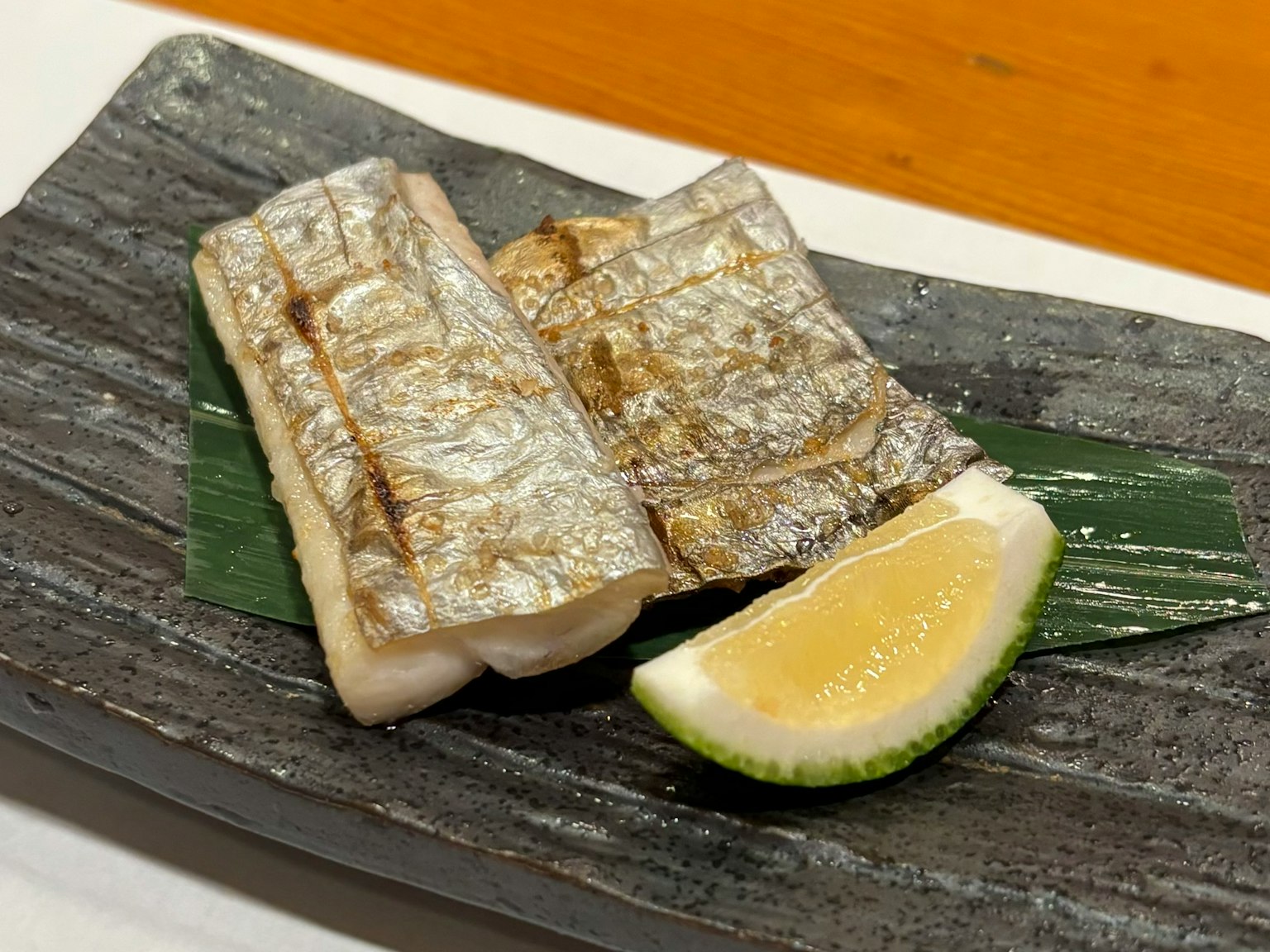 黑色盘子上盛着烤鱼片和一片柠檬