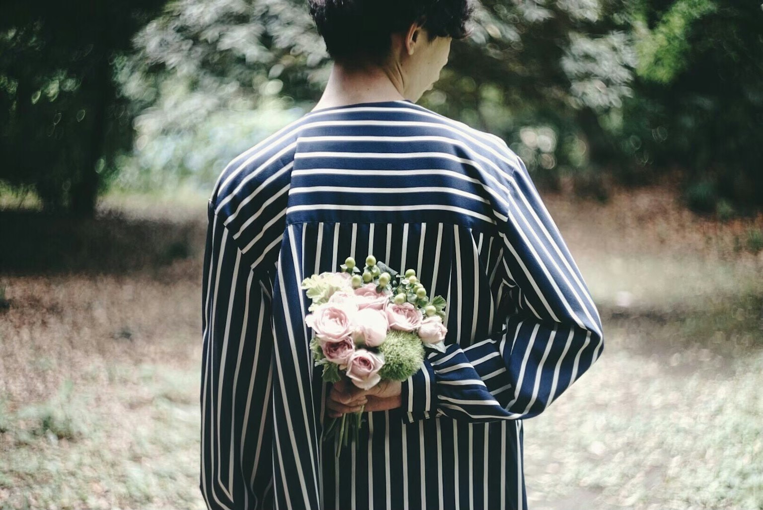 穿著條紋襯衫的人把花束藏在背後