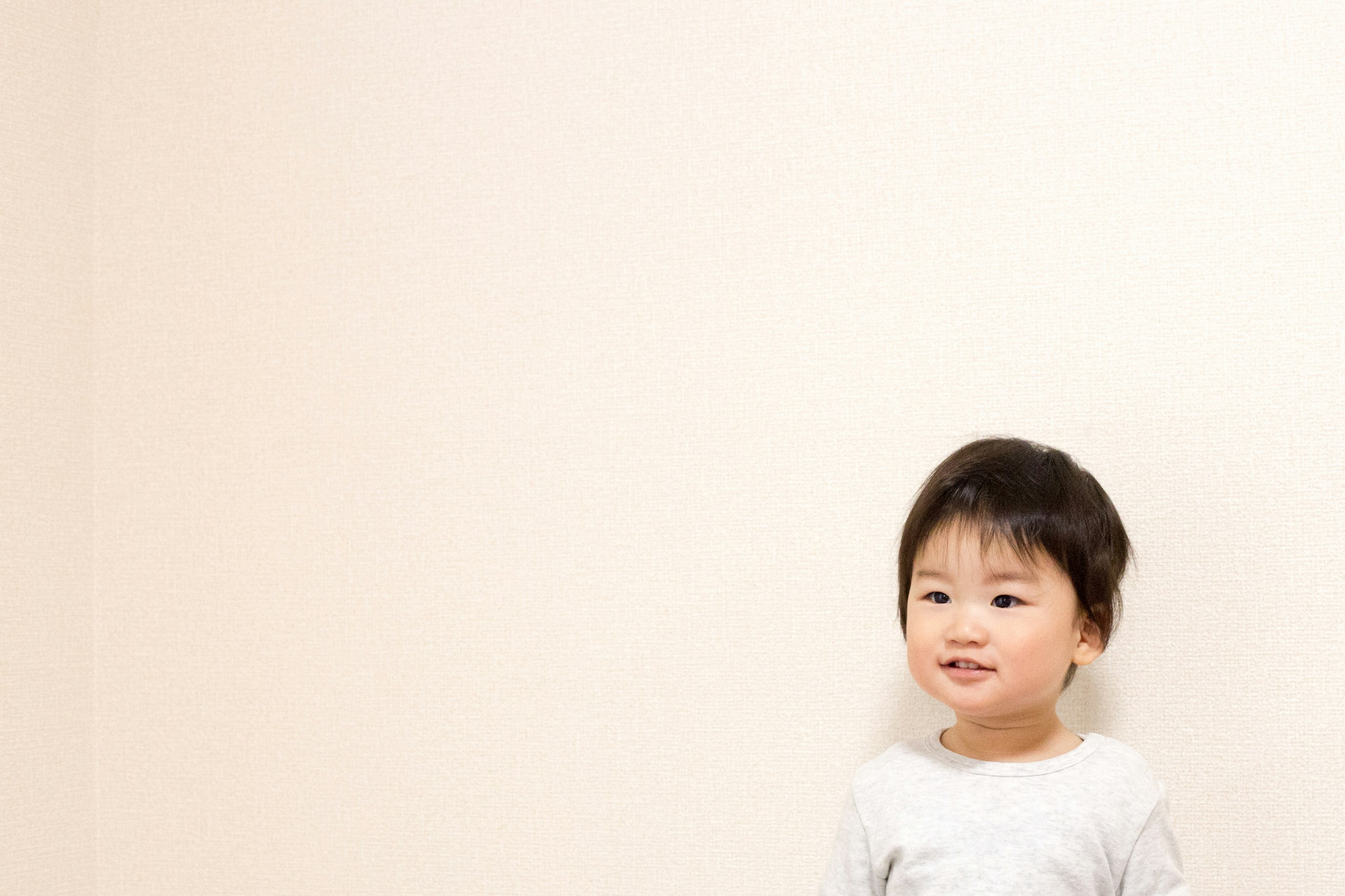 niño pequeño sonriente de pie frente a una pared lisa