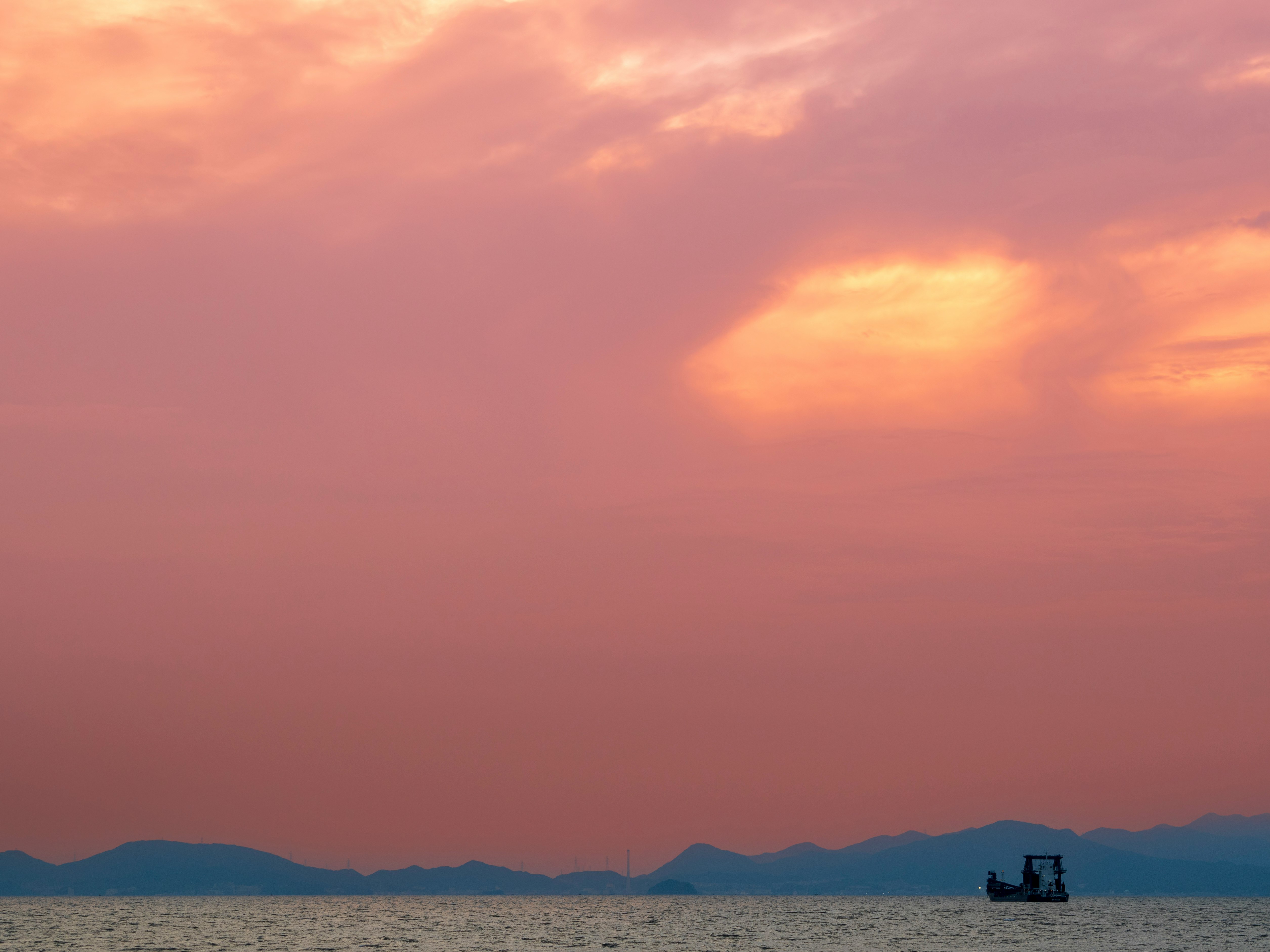 夕焼けの海と水平線、沖合の小さな船