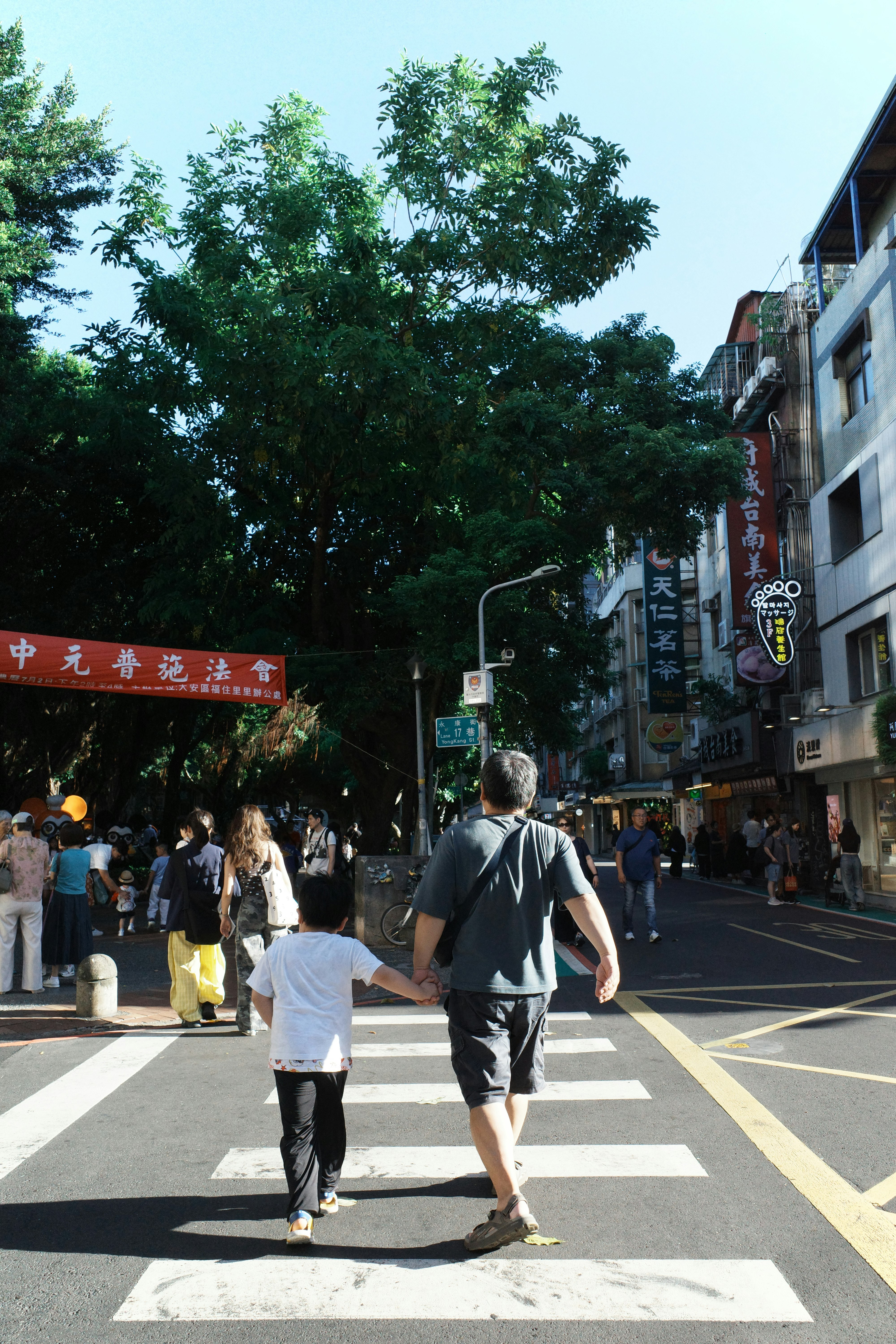 交差点を渡る親子の後ろ姿が見える街の通り