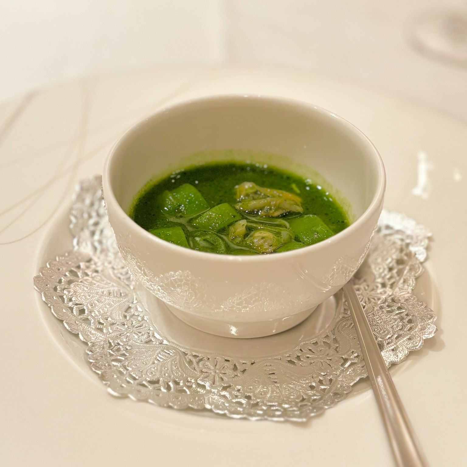 Zuppa verde in una ciotola bianca posata su un piatto in pizzo delicato