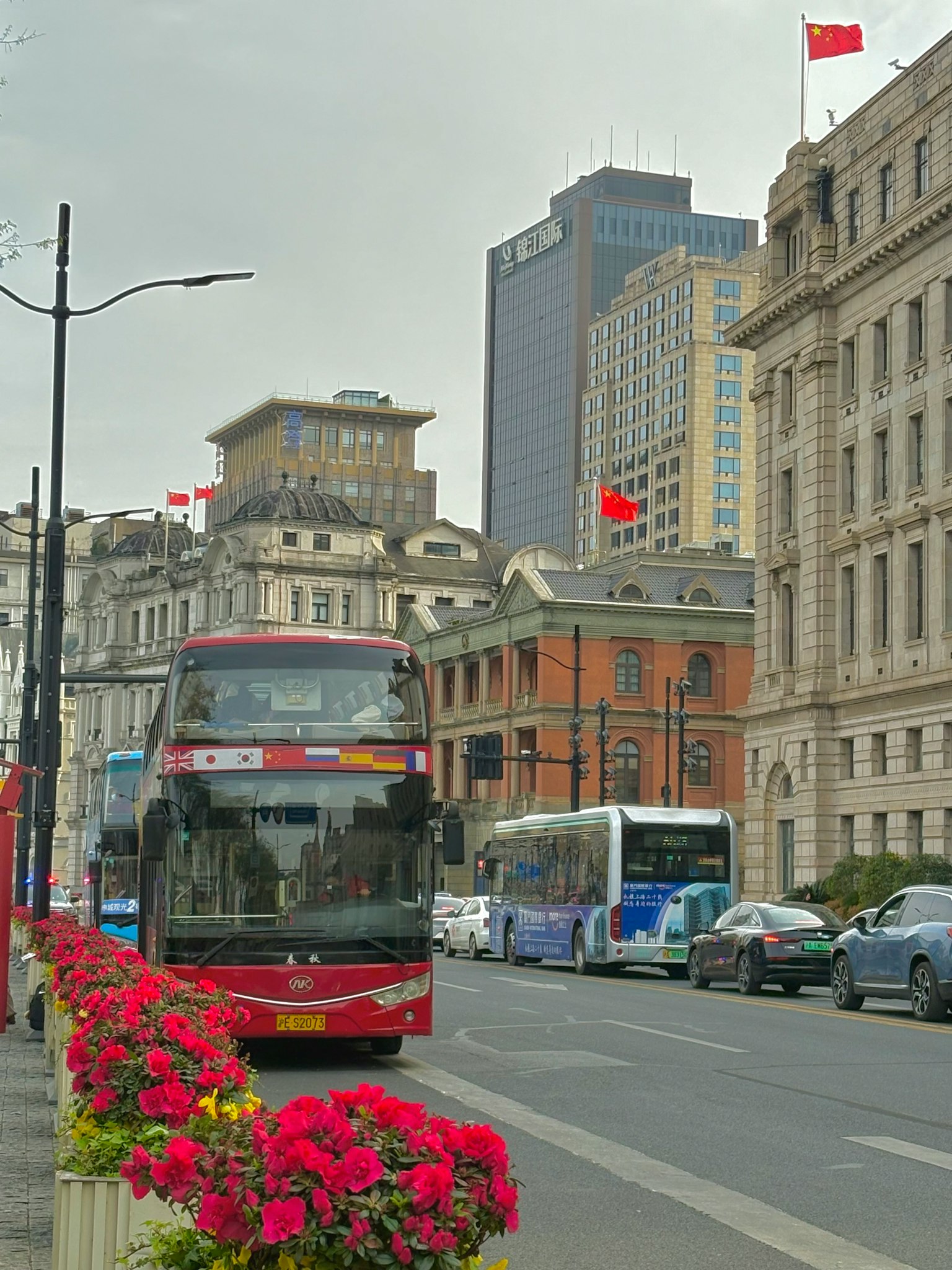 Vista di strada con un autobus rosso e aiuole di fiori grattacieli e bandiere sullo sfondo
