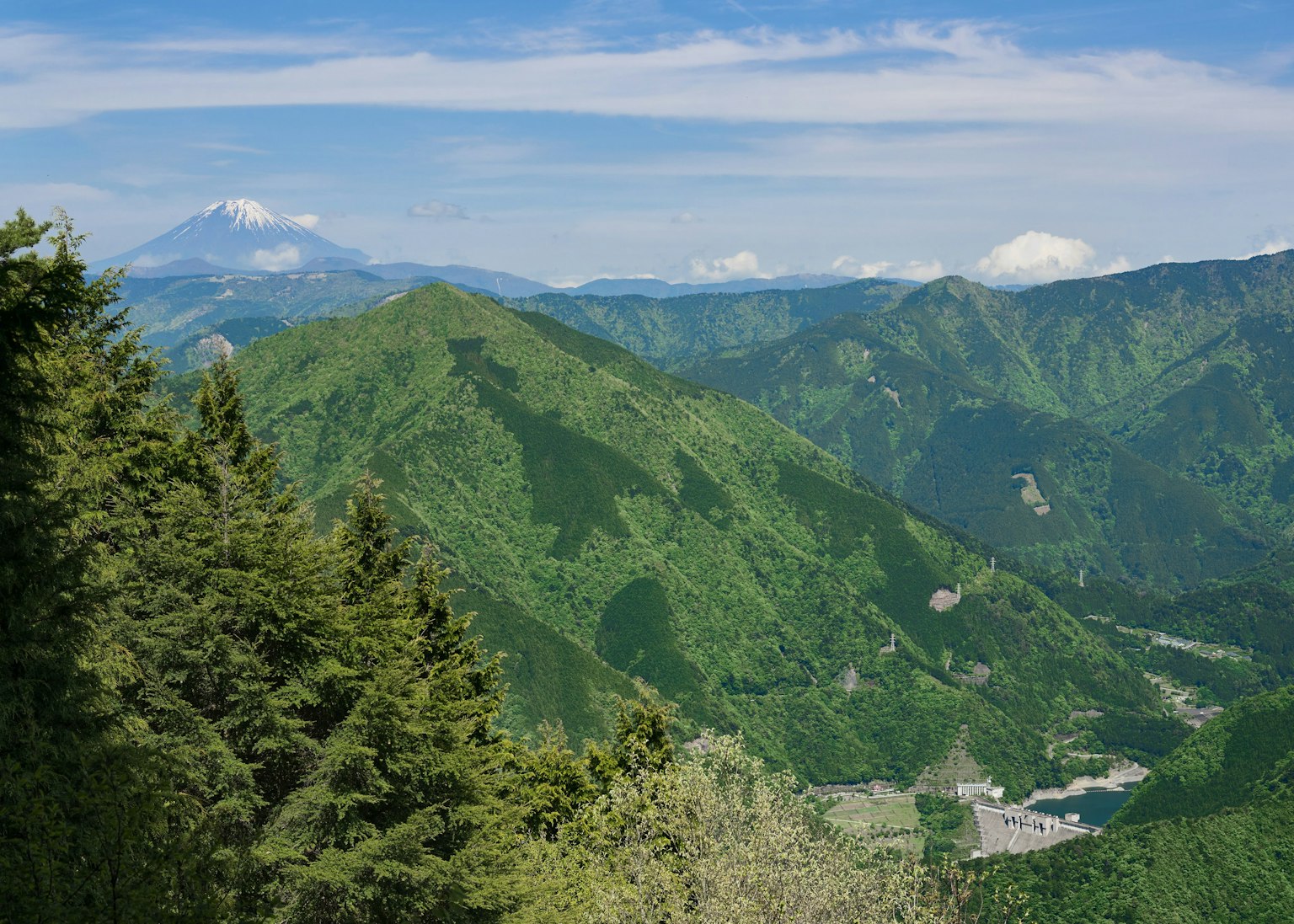 Lush green mountains with a clear blue sky and Mount Fuji in the distance