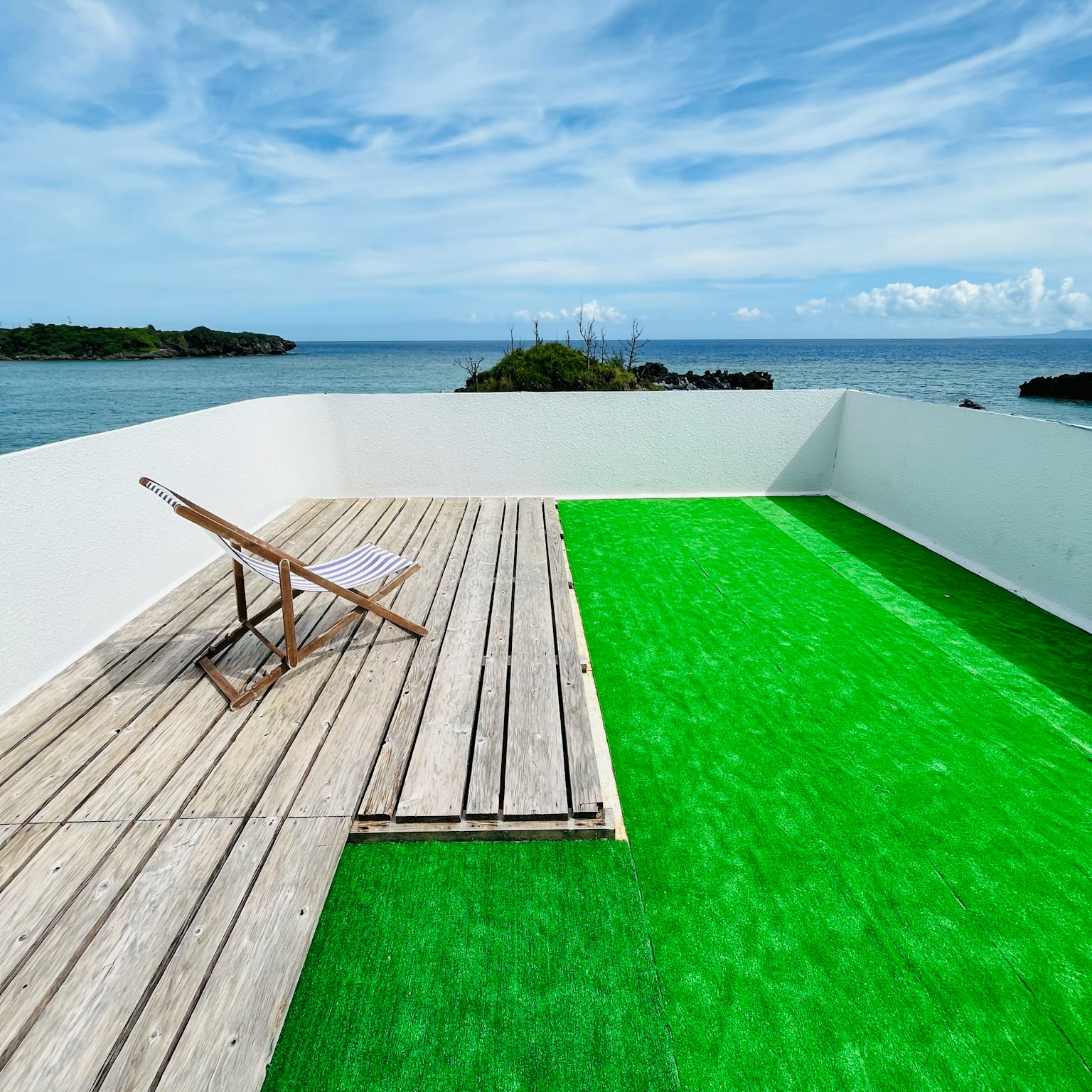 Atap dengan rumput hijau dan dek kayu yang menghadap ke laut biru dan langit