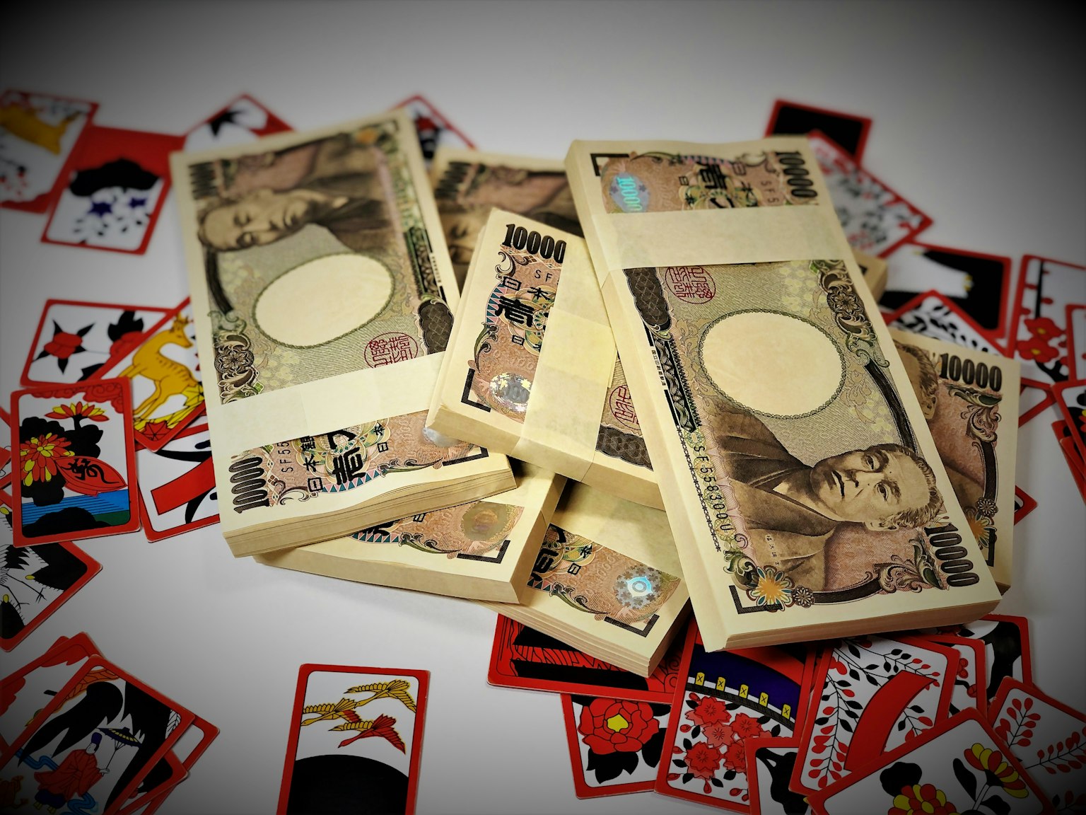 Gambar yang menampilkan tumpukan mata uang Jepang dikelilingi oleh kartu bermain berwarna