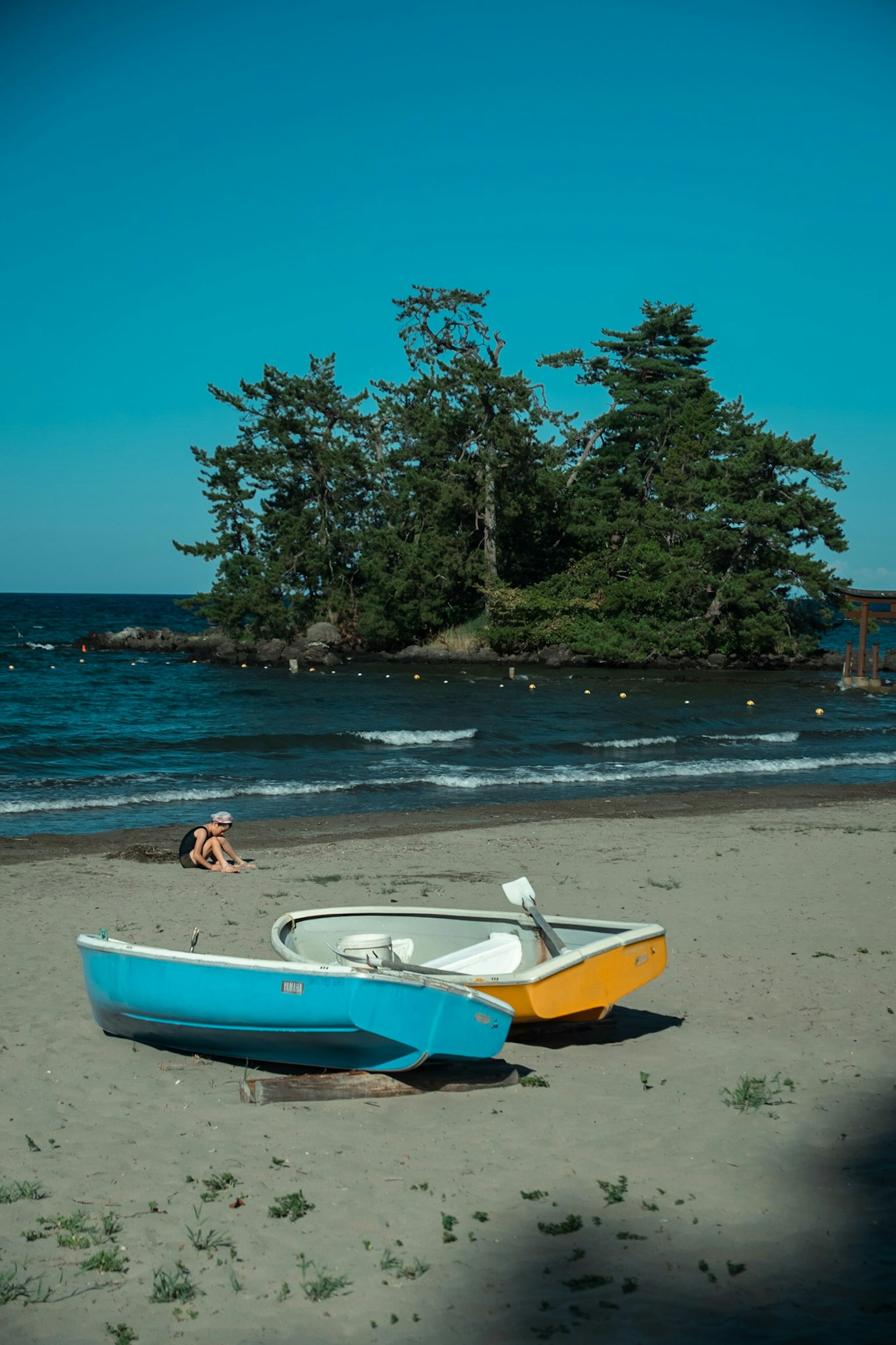 Zwei Boote an einem Sandstrand unter einem blauen Himmel mit einer kleinen Insel im Hintergrund