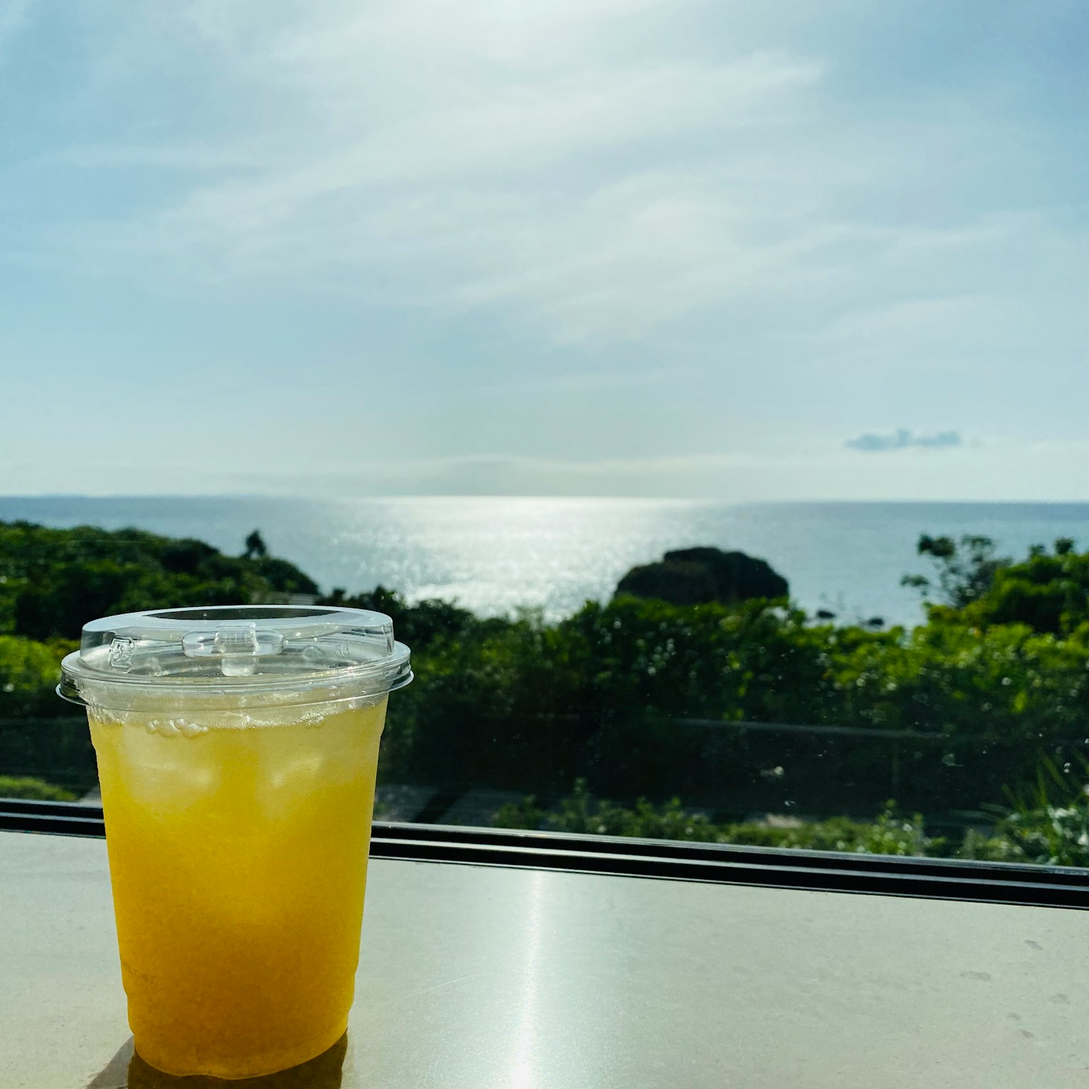 Gelas transparan dengan minuman dan pemandangan laut