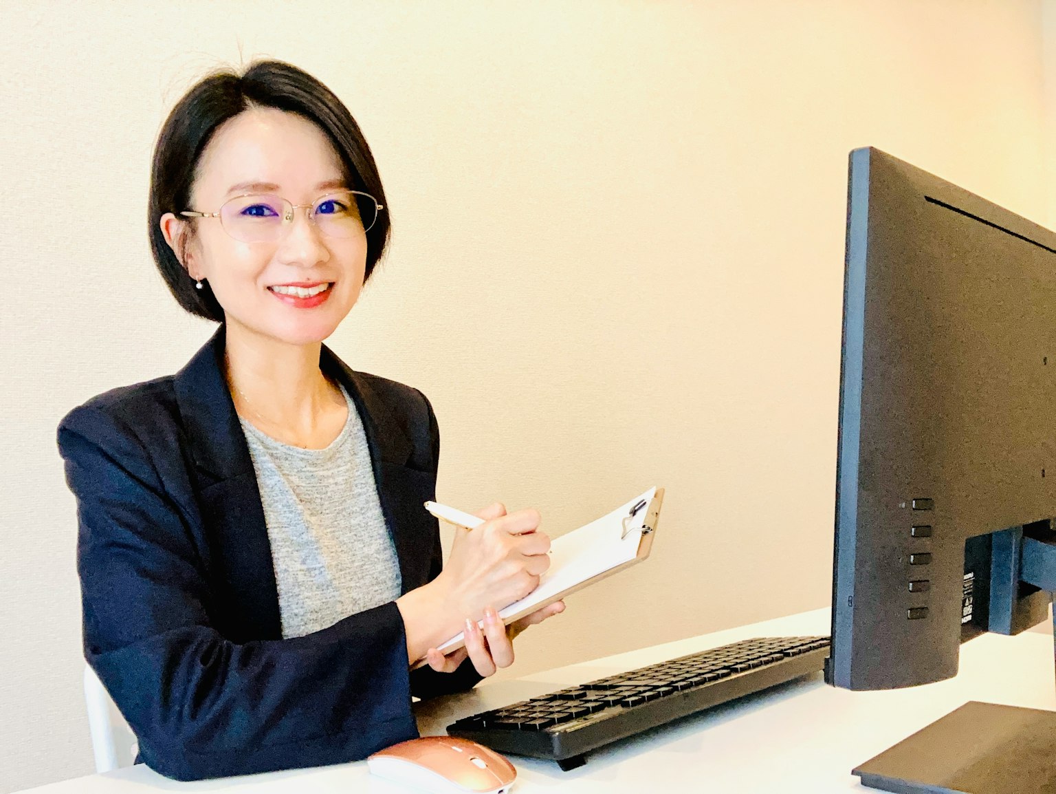 Người phụ nữ mỉm cười ghi chú tại bàn làm việc với máy tính trong bối cảnh kinh doanh