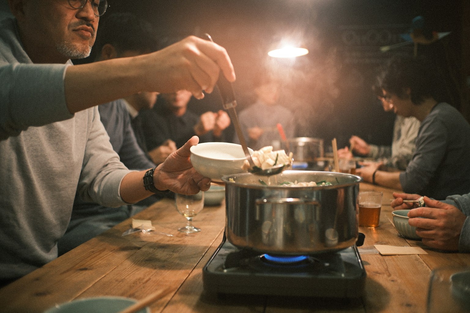 温かい鍋料理を囲む人々の集まり 食卓に置かれた鍋と食材 蒸気が立ち上る