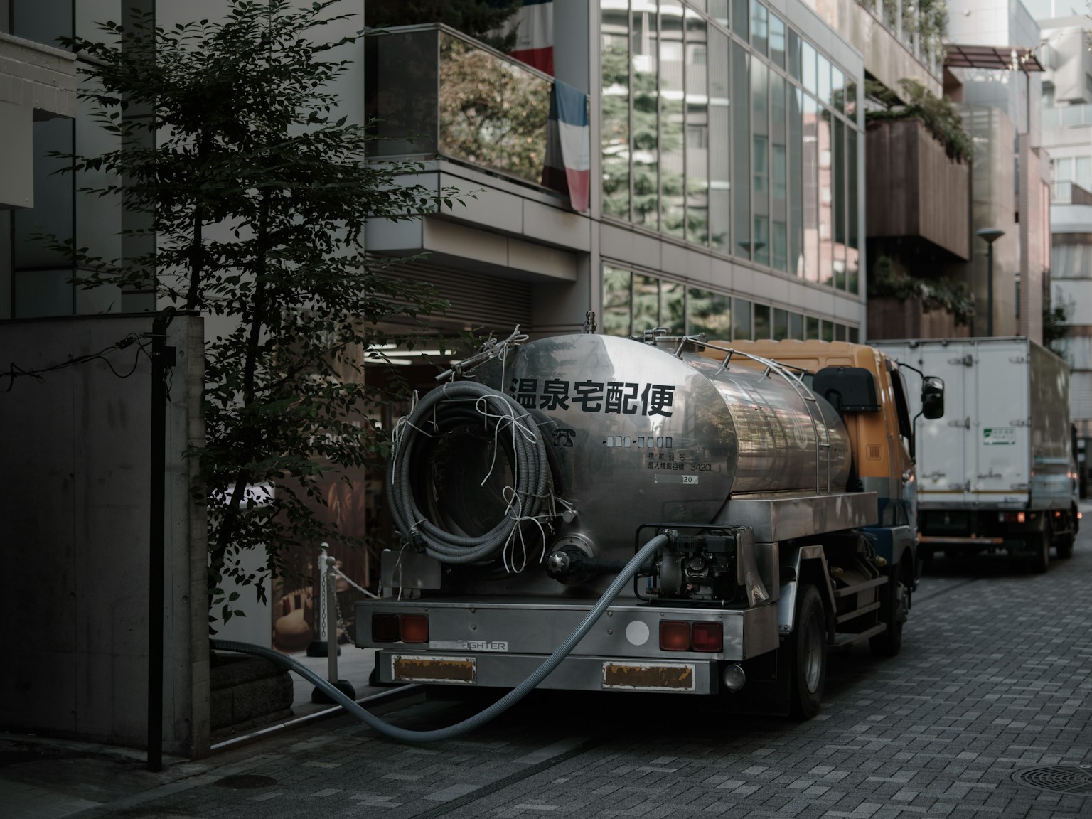 一辆银色的油罐车停在狭窄的街道上，背景是现代建筑