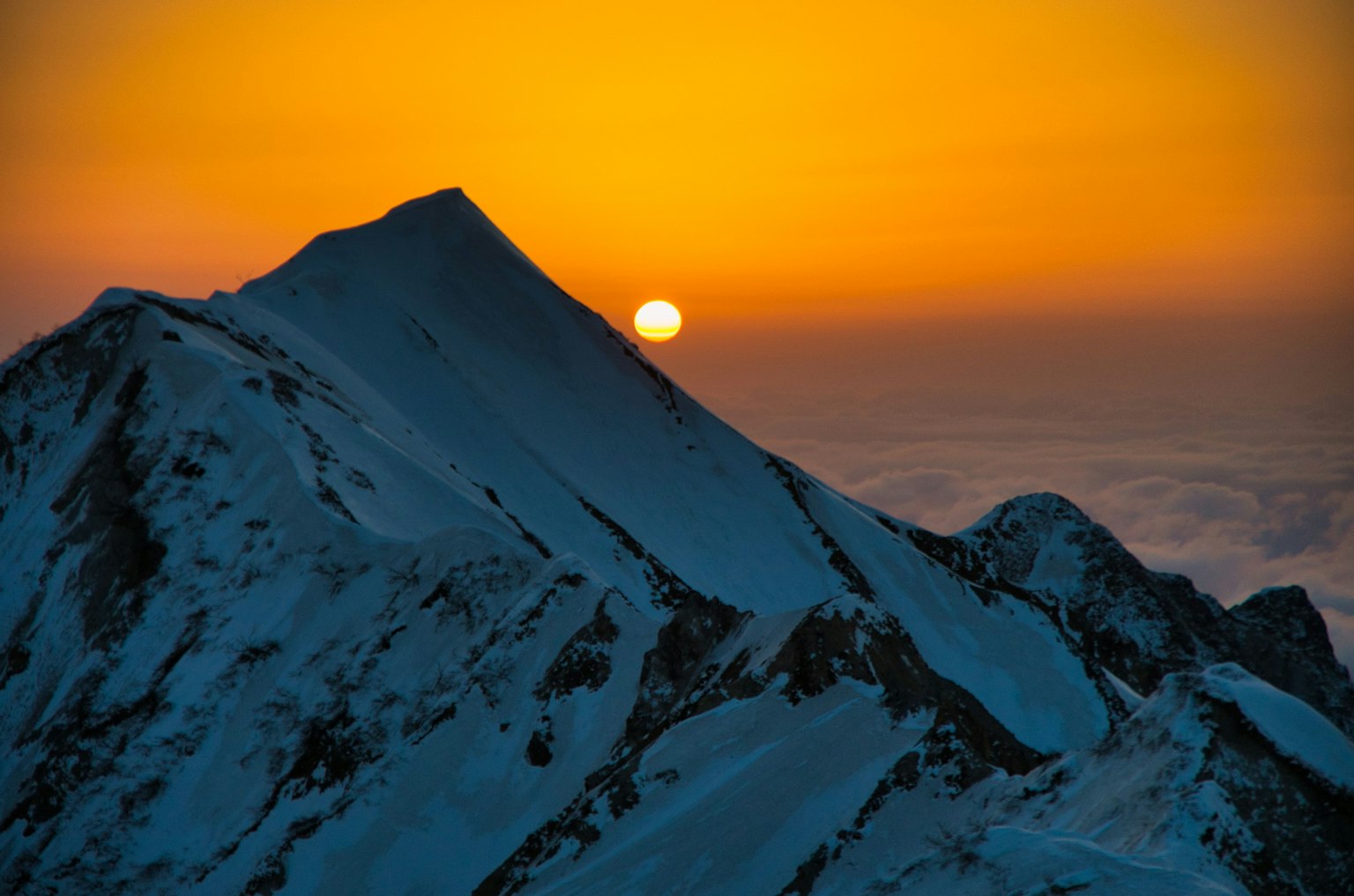 Schneebedeckter Berggipfel mit orangefarbenem Sonnenuntergang