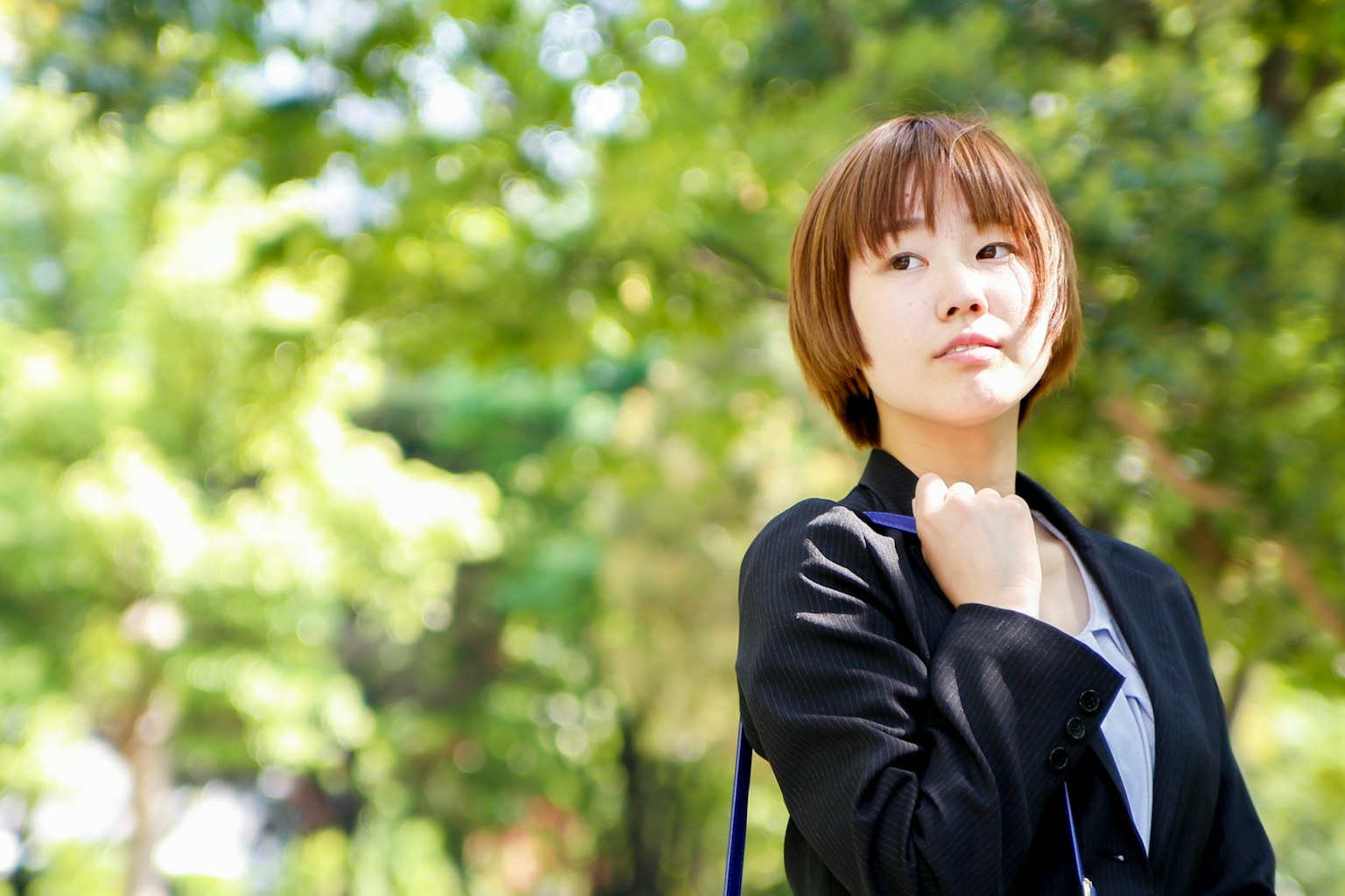 Woman in a park contemplating with a green background short hairstyle wearing a black jacket