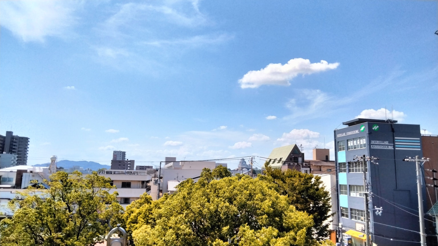 ทิวทัศน์เมืองท้องฟ้าสีฟ้าและเมฆขาวต้นไม้เขียวและอาคาร